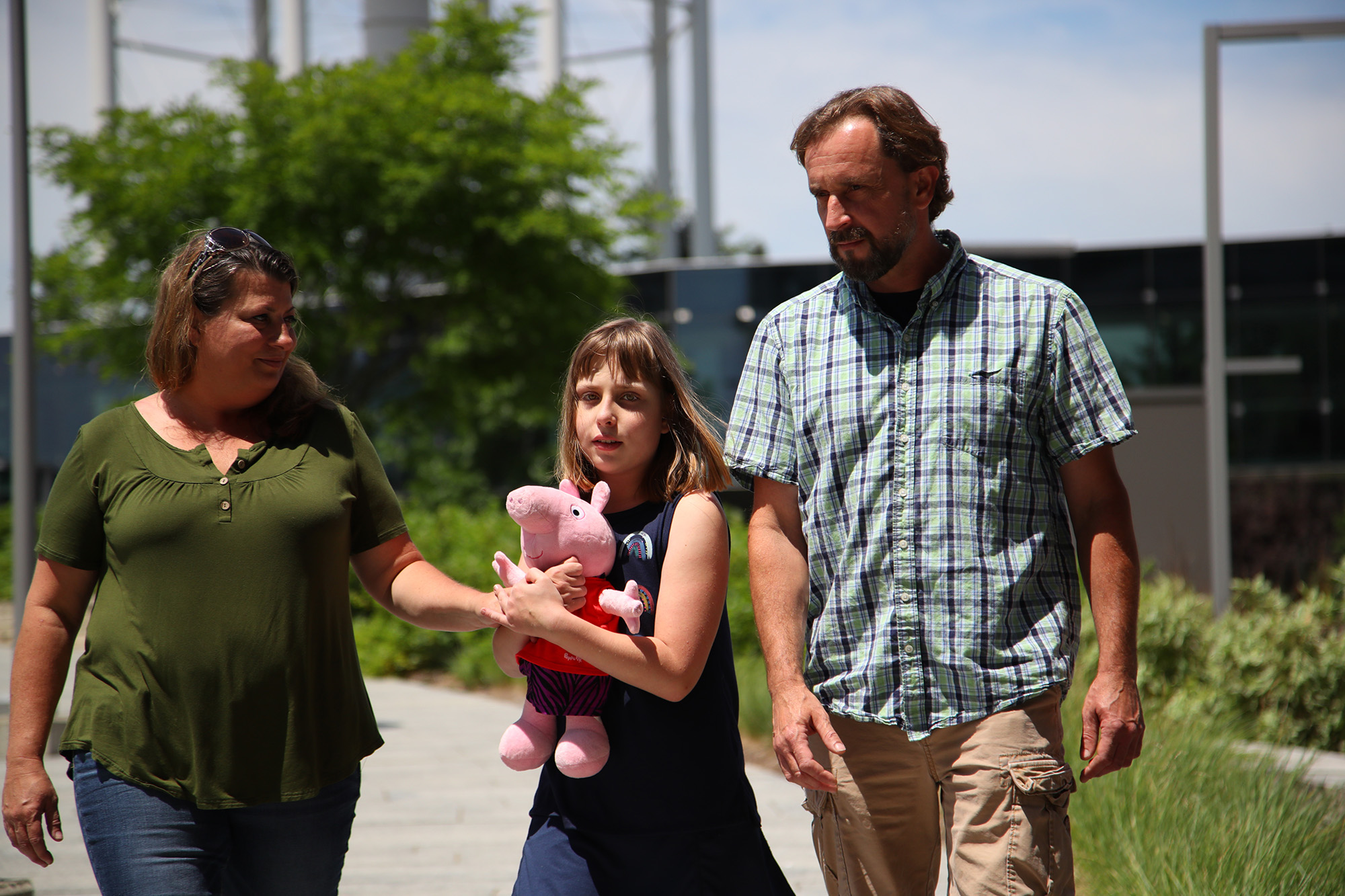 a young girl holding a stuffed animal walking with her parents