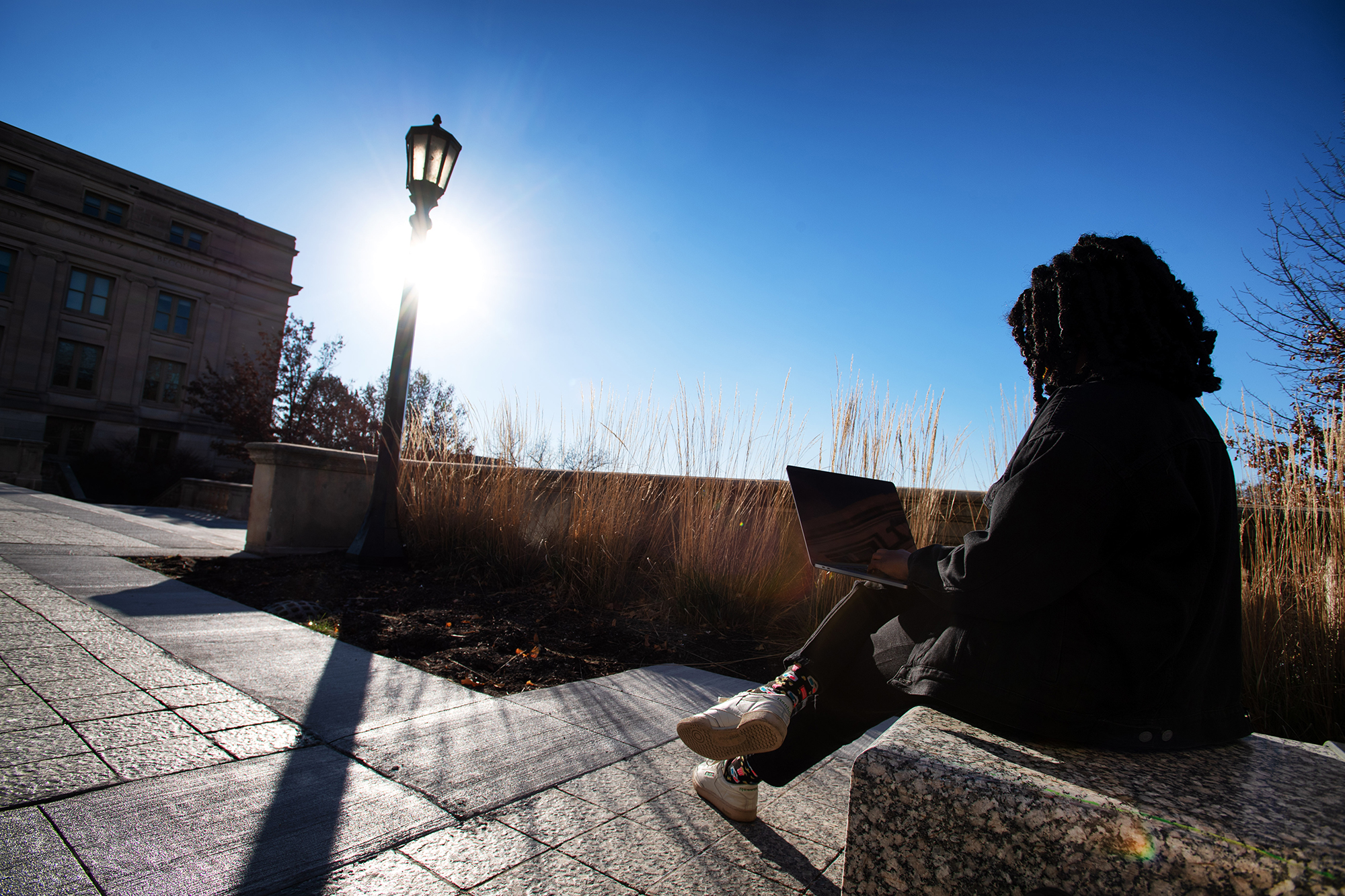 a student sitting on the university of iowa campus writing on a laptop computer