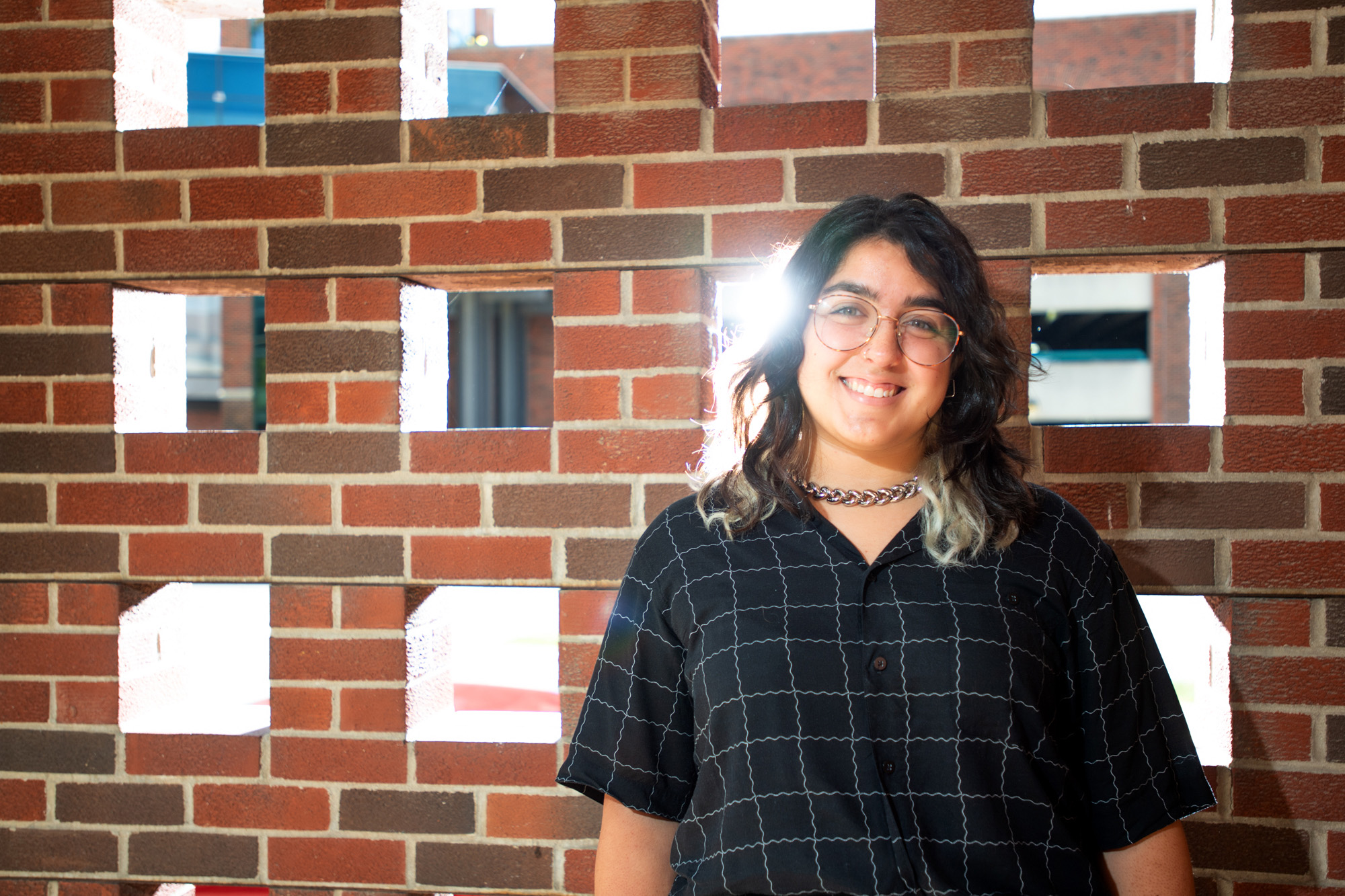 University of Iowa graduate student Bianca Robles-Munoz standing near a brick wall with sunlight coming through openings