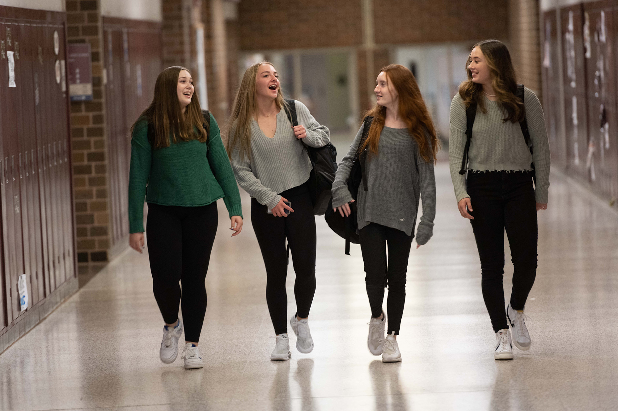four girls talk and laugh while walking through a school hallway