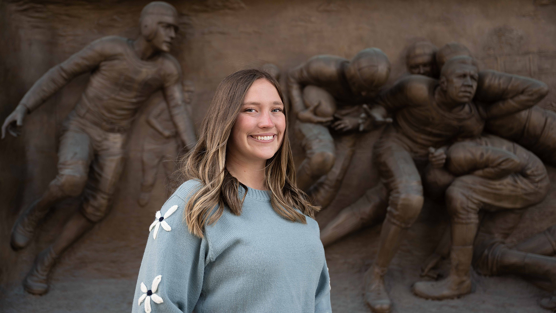 a woman standing in front of a sculpture featuring football players