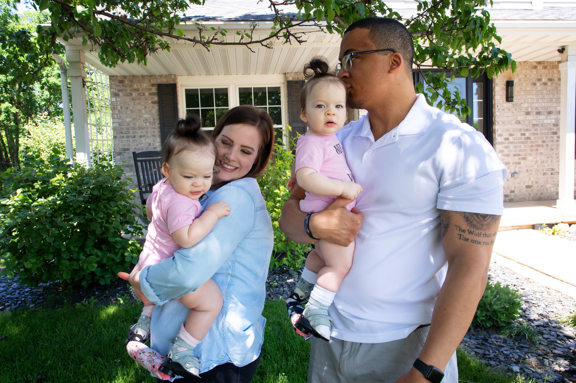 the McDaniel family stands outdoors at their home; each parent holds one of the twin girls