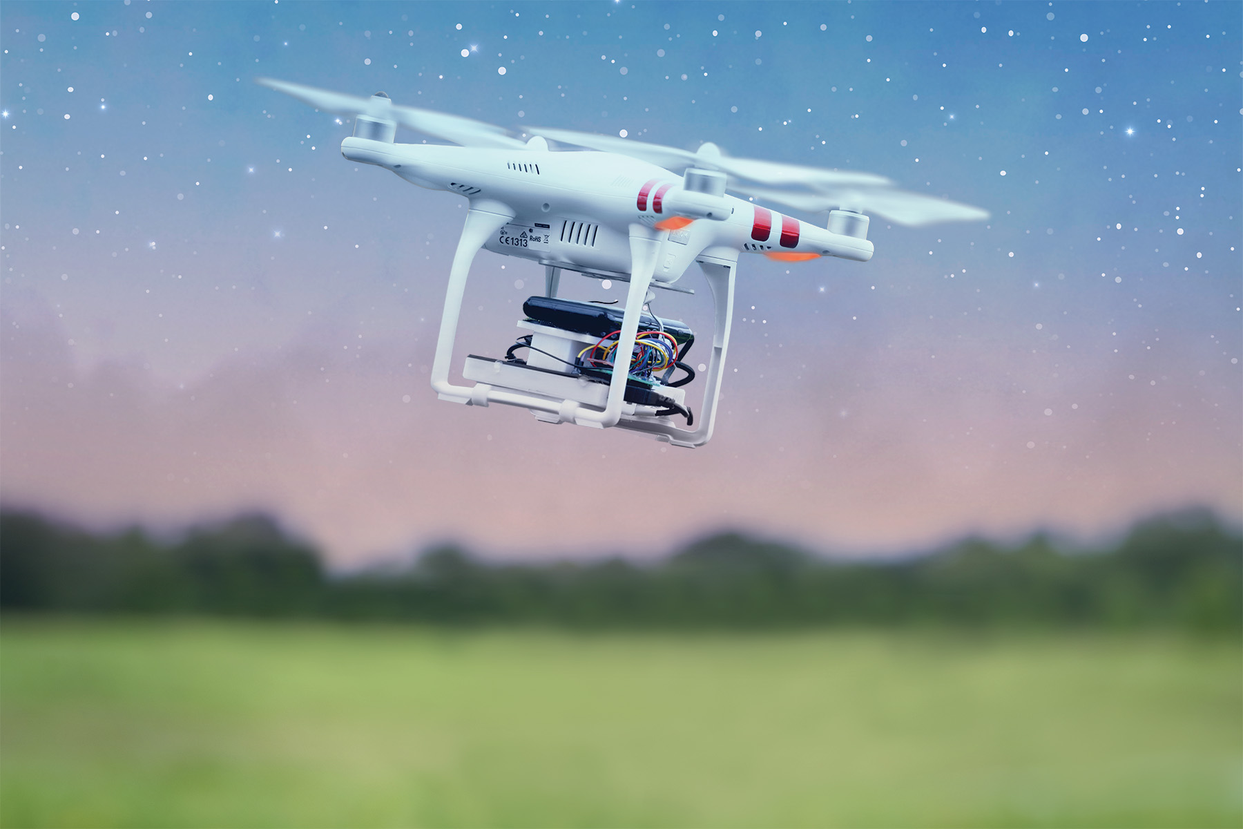 a drone flying amid a star-filled sky in a grassy and wooded landscape