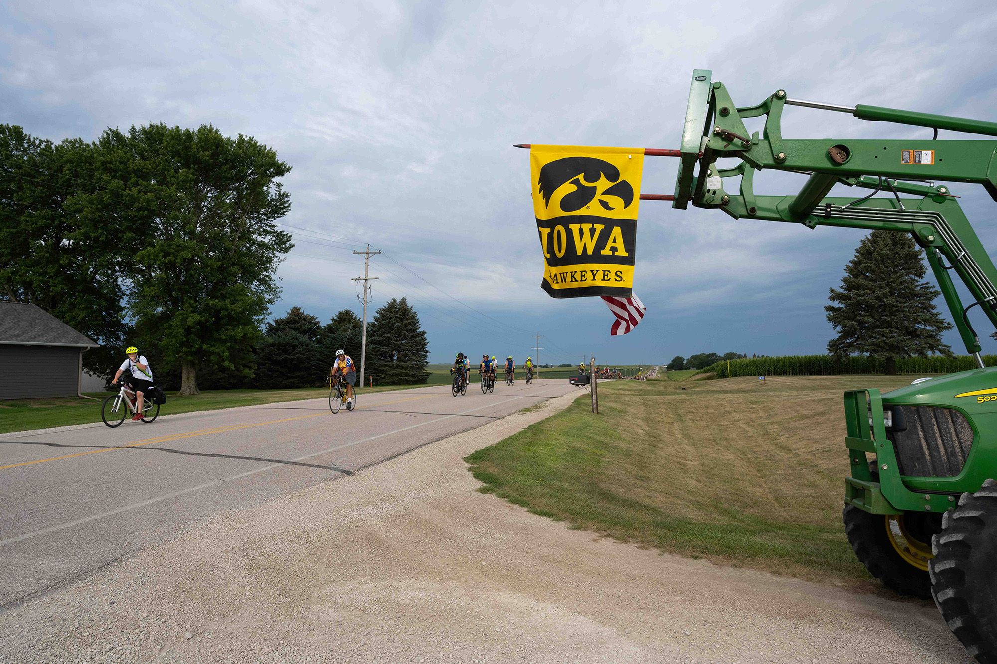 RAGBRAI riders pass by farm equipment flying an Iowa Hawkeyes flag