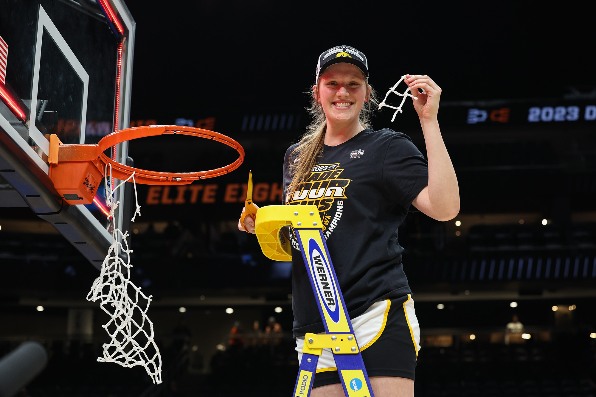 University of Iowa women's basketball player Sharon Goodman standing on a ladder holding a strand of netting after a basketball game
