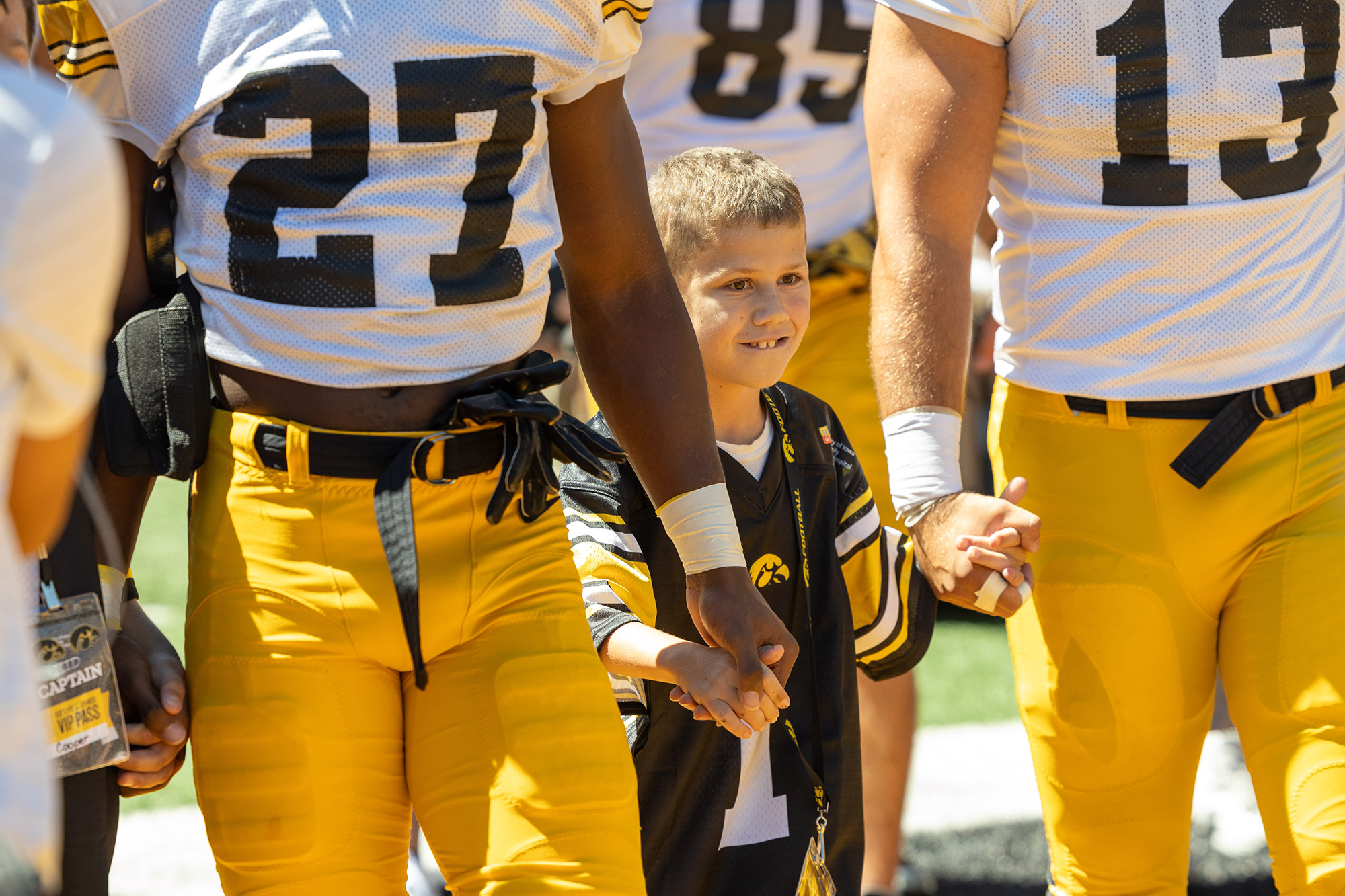 Kid Captain Wyatt Rannals stands between two football players, holding their hands