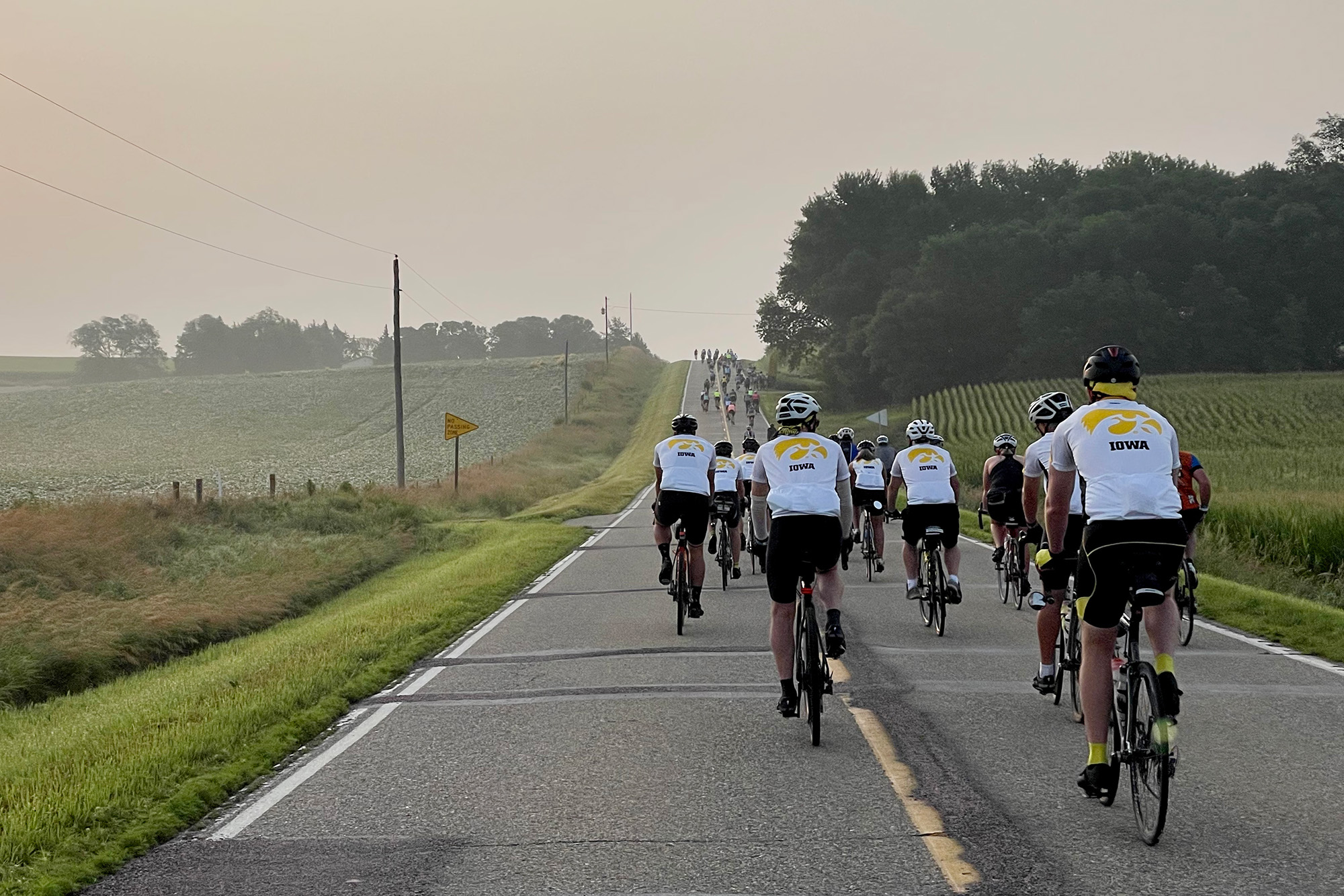 riders wearing gear adorned with Tiger hawk logos travel down a scenic country road during RAGBRAI