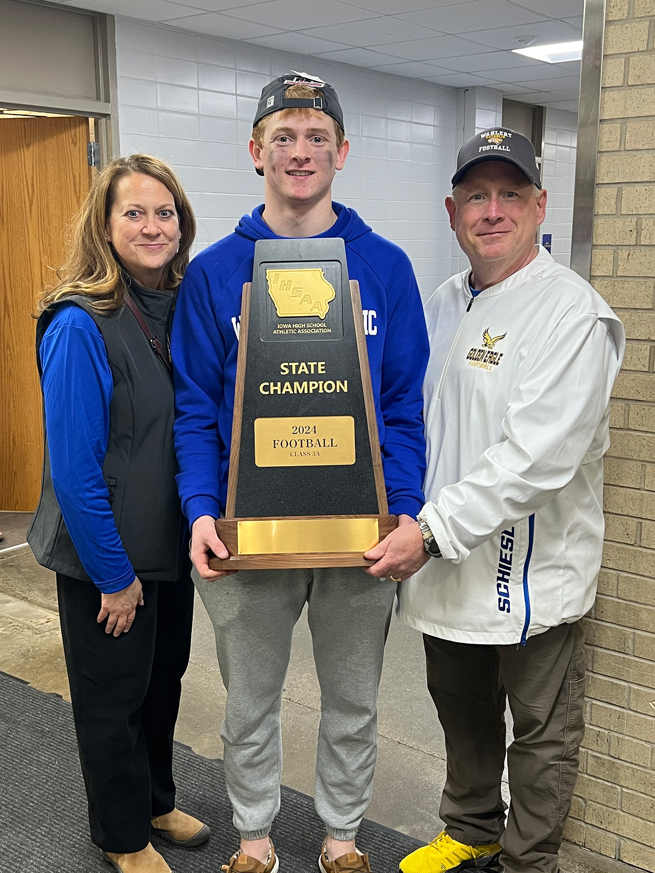 a high school football player and his parents posing with a state champions trophy