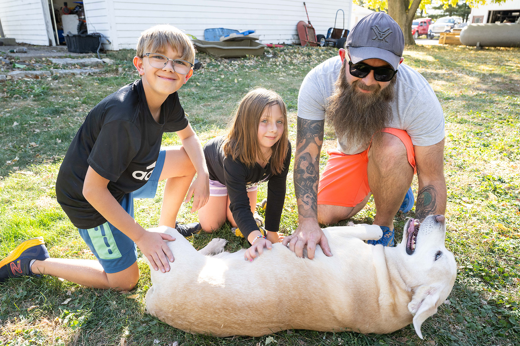 a dad and his two kids petting the family dog 