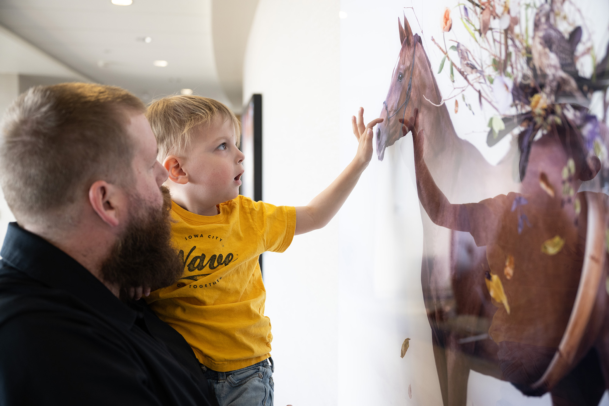 A father holding up his young son as e looks at a picture of a horse