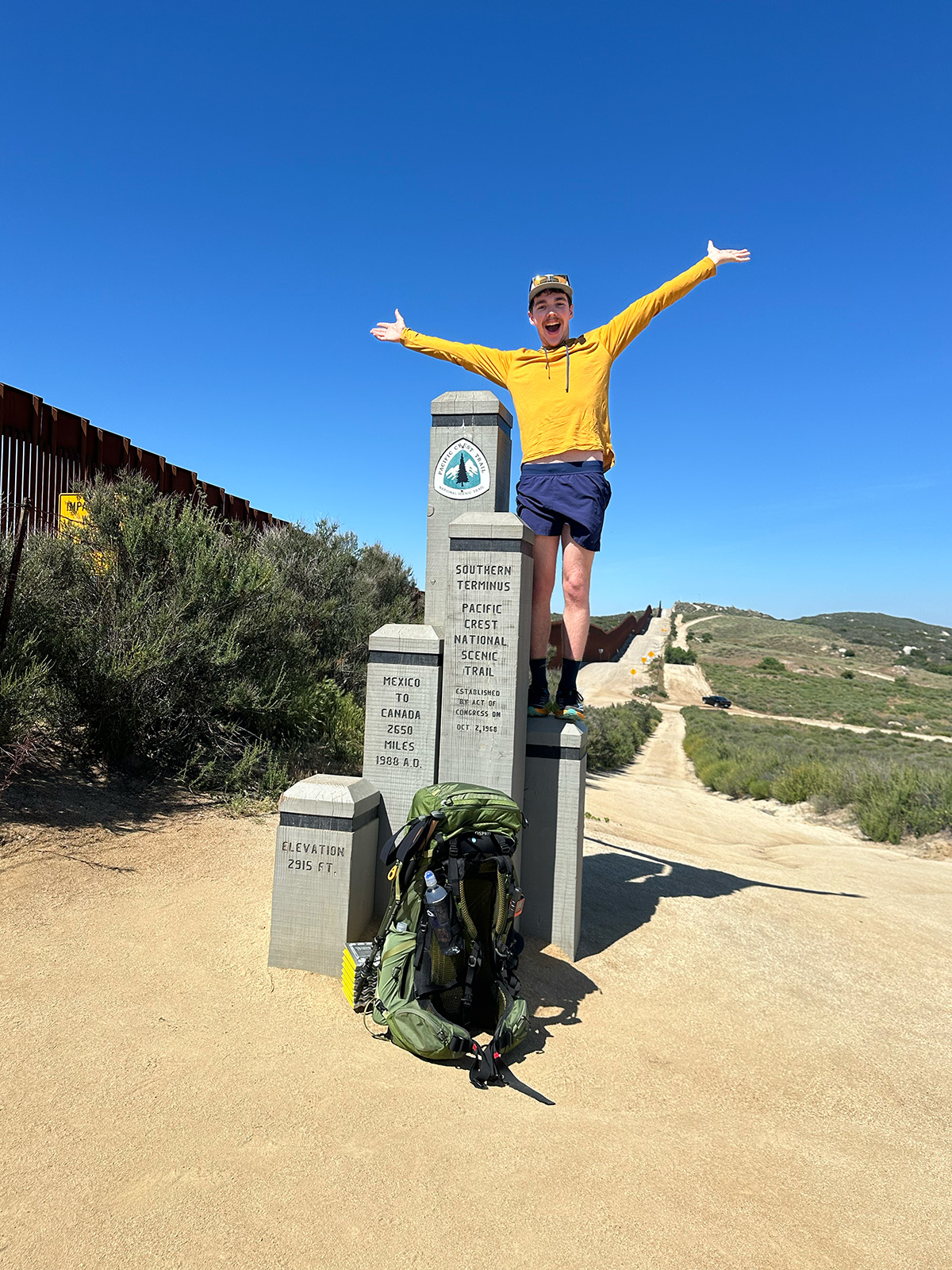 a man stands atop a marker that denotes the southernmost point of the Pacific Crest Trail