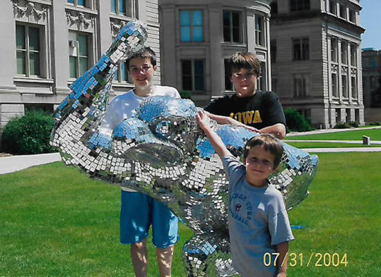 Three young boys posing in-front of a shining statue of herky
