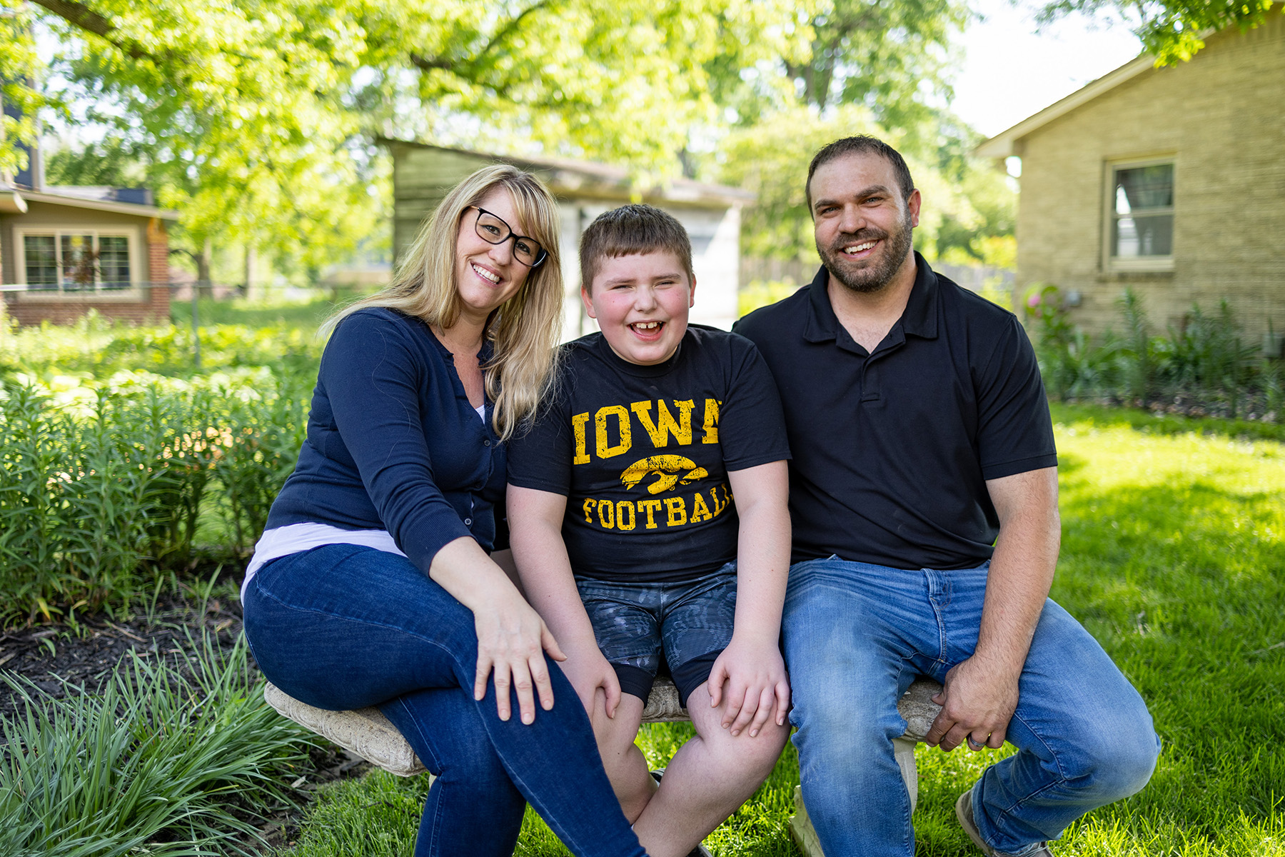 A boy and his parents sitting on a bench outside smiling
