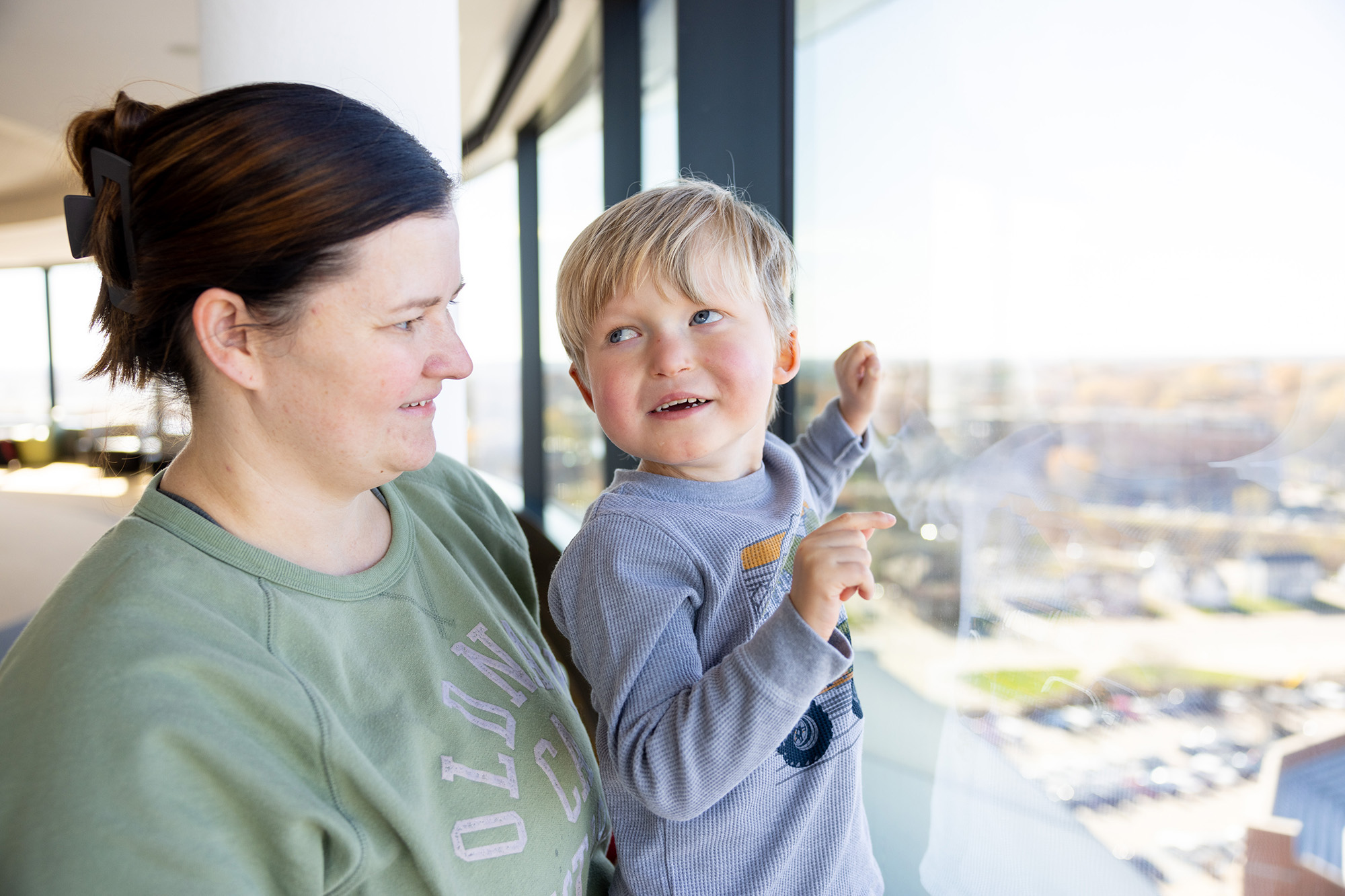 A woman holding up her son to look out a window