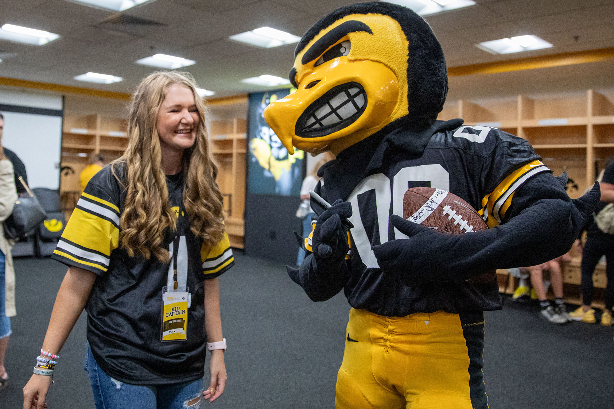 A girl laughing at a bird mascot with a football