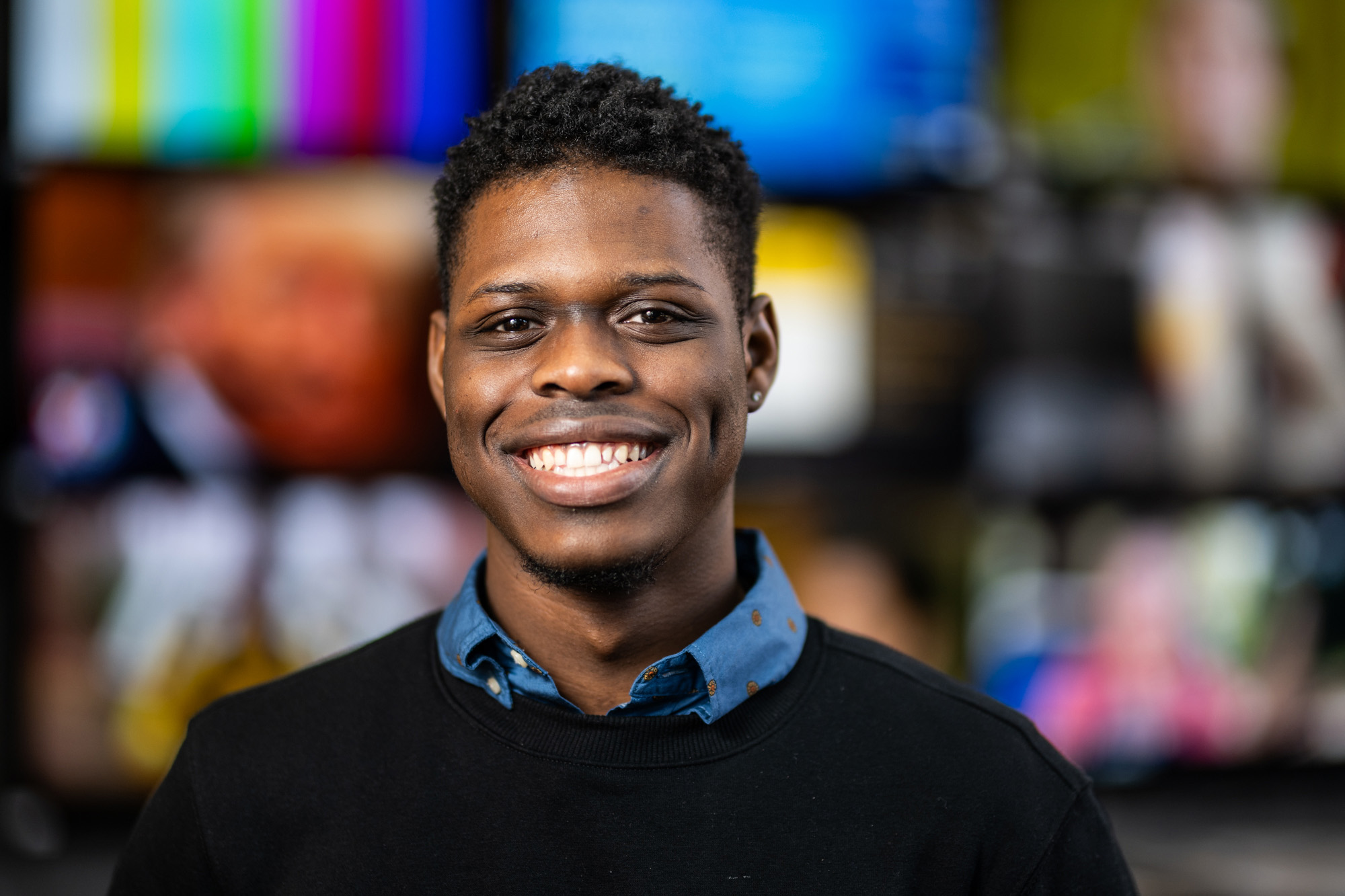 A man smiling with multiple TV monitors behind him