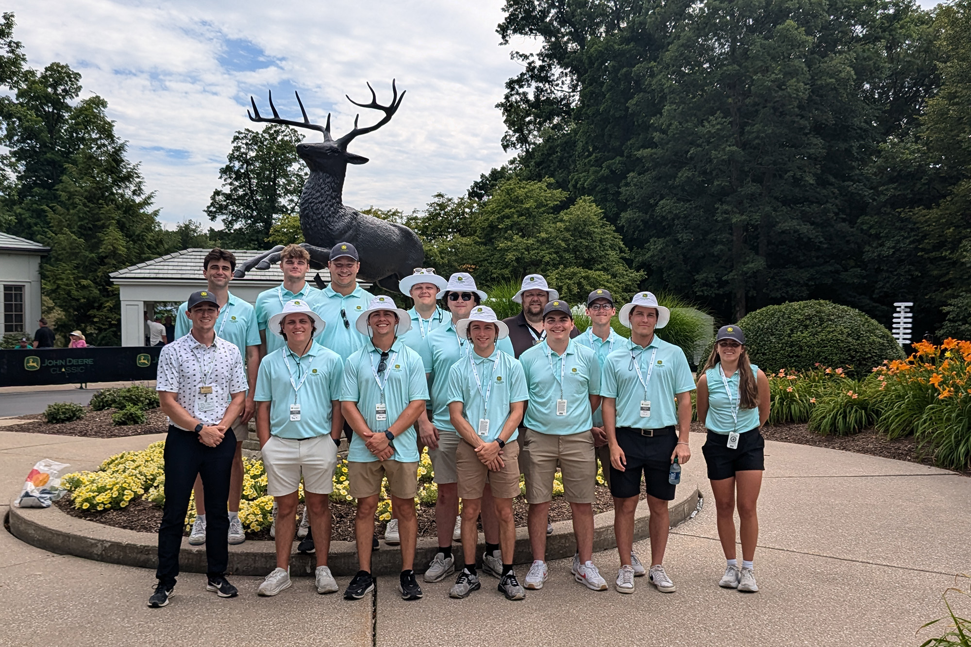 A group of golf course workers standing together in front of a deer statue