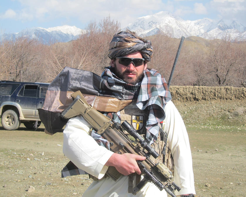 A soldier standing in a field holding a gun across his chest