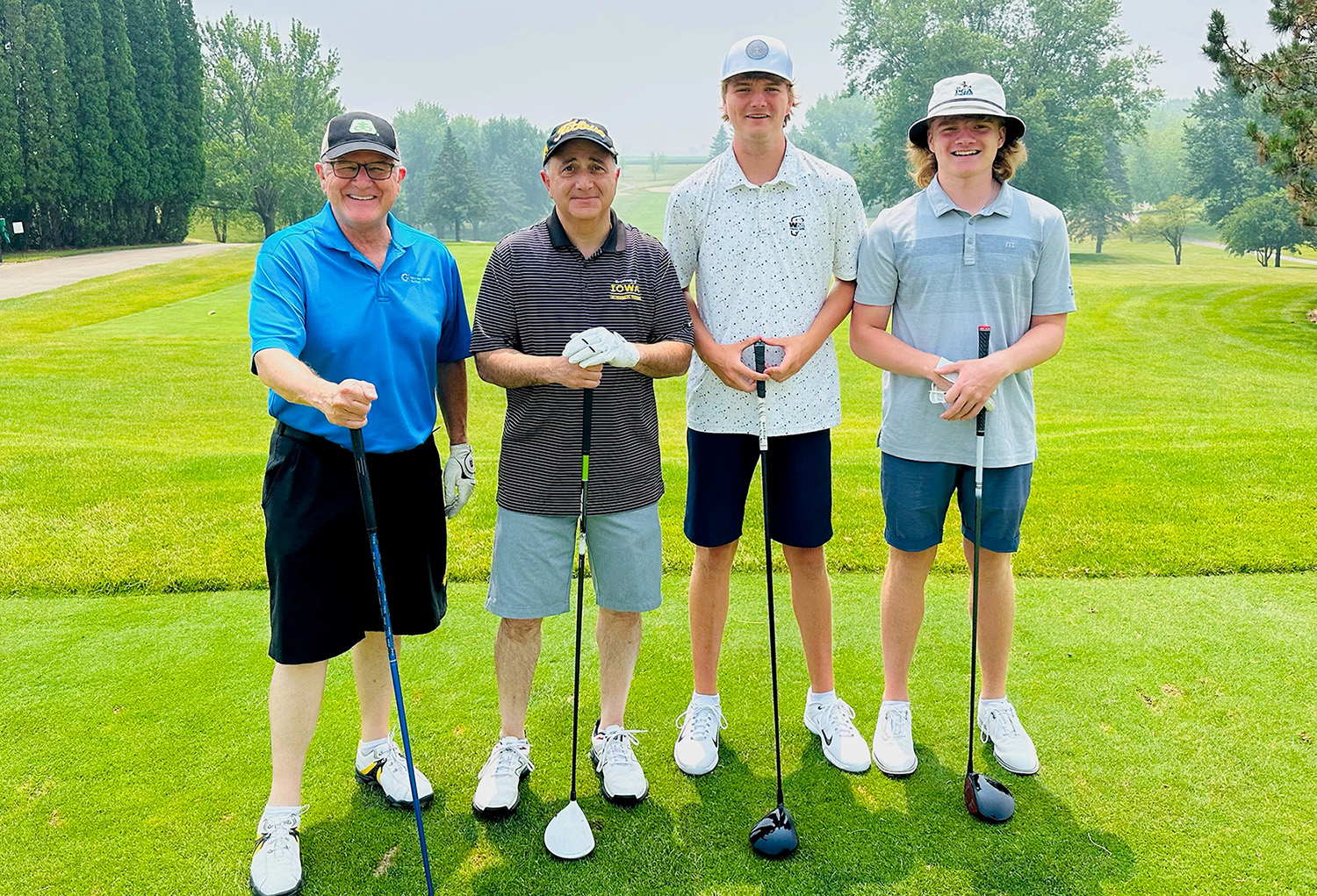 Four men standing together holding golf clubs