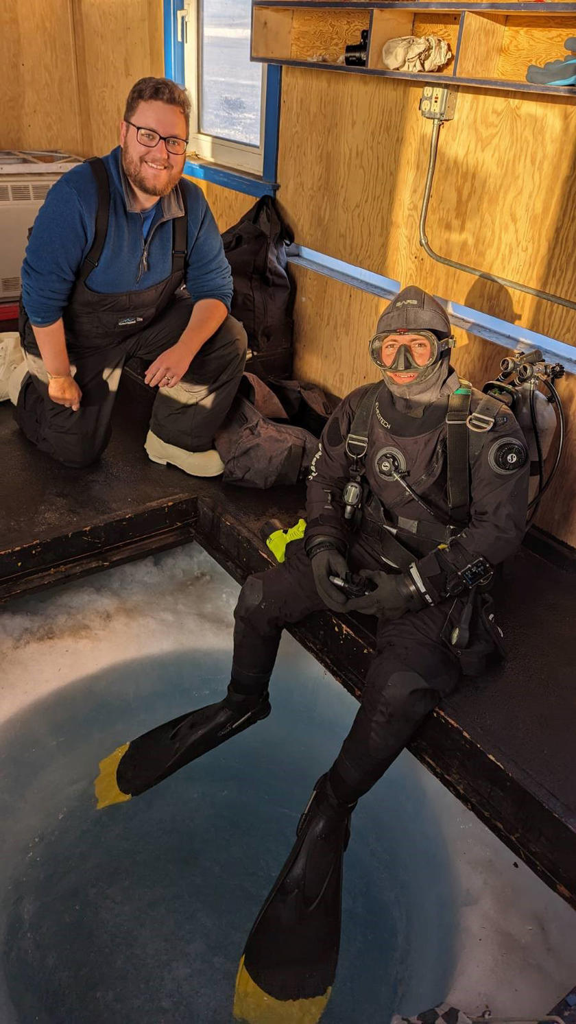 A man kneeling on a platform while another person sits on the ledge in diving gear