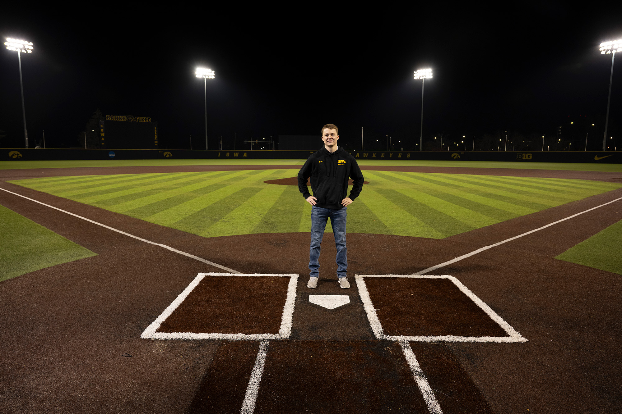 A man standing at home plate with a baseball field behind him