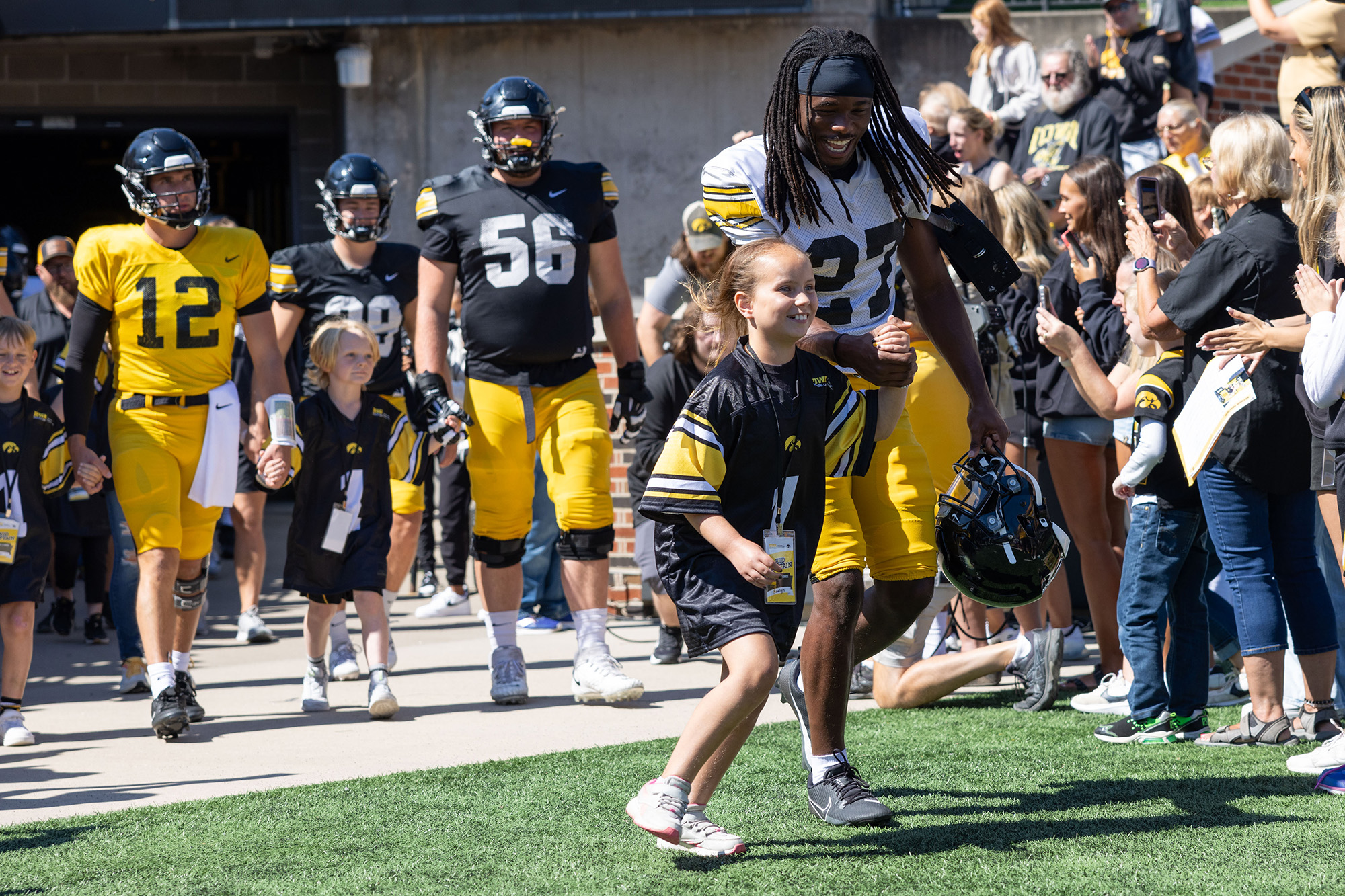 A young girl running onto a football field with a football player
