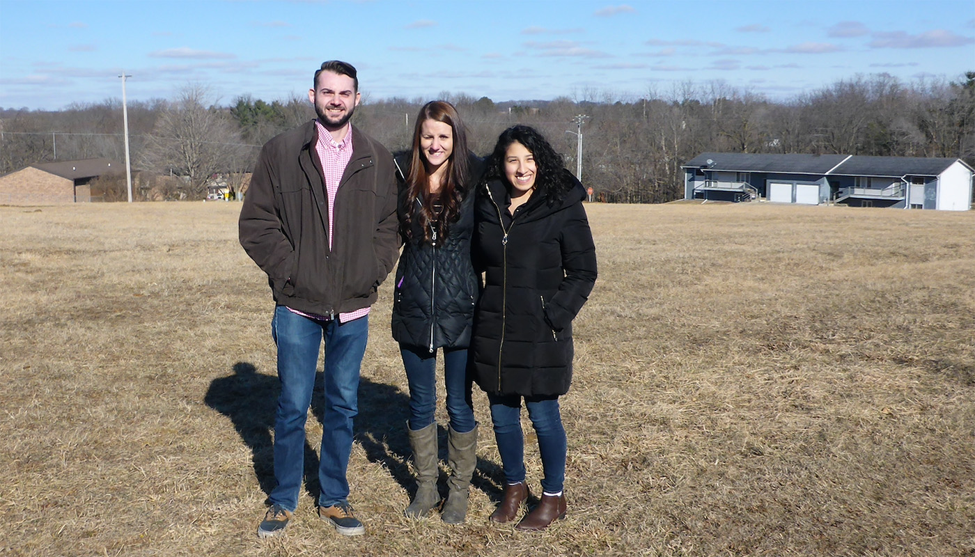 Then-University of Iowa engineering students Tanner Schropp, Morgan Kinney, and Mayra Corona stand in the spot that would become the Bear River Cottages development in Maquoketa, Iowa.