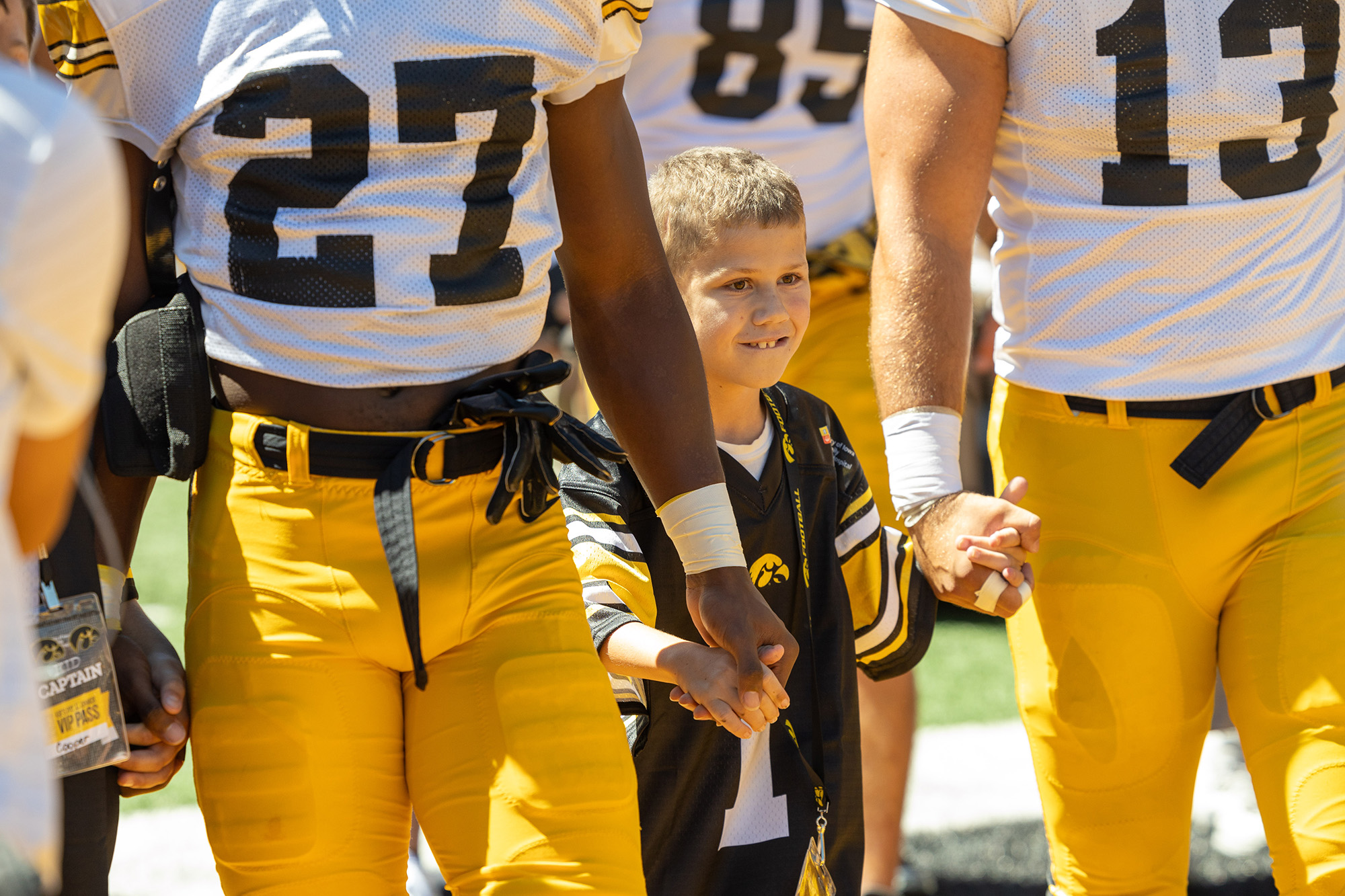 A young boy holding hands with two football players