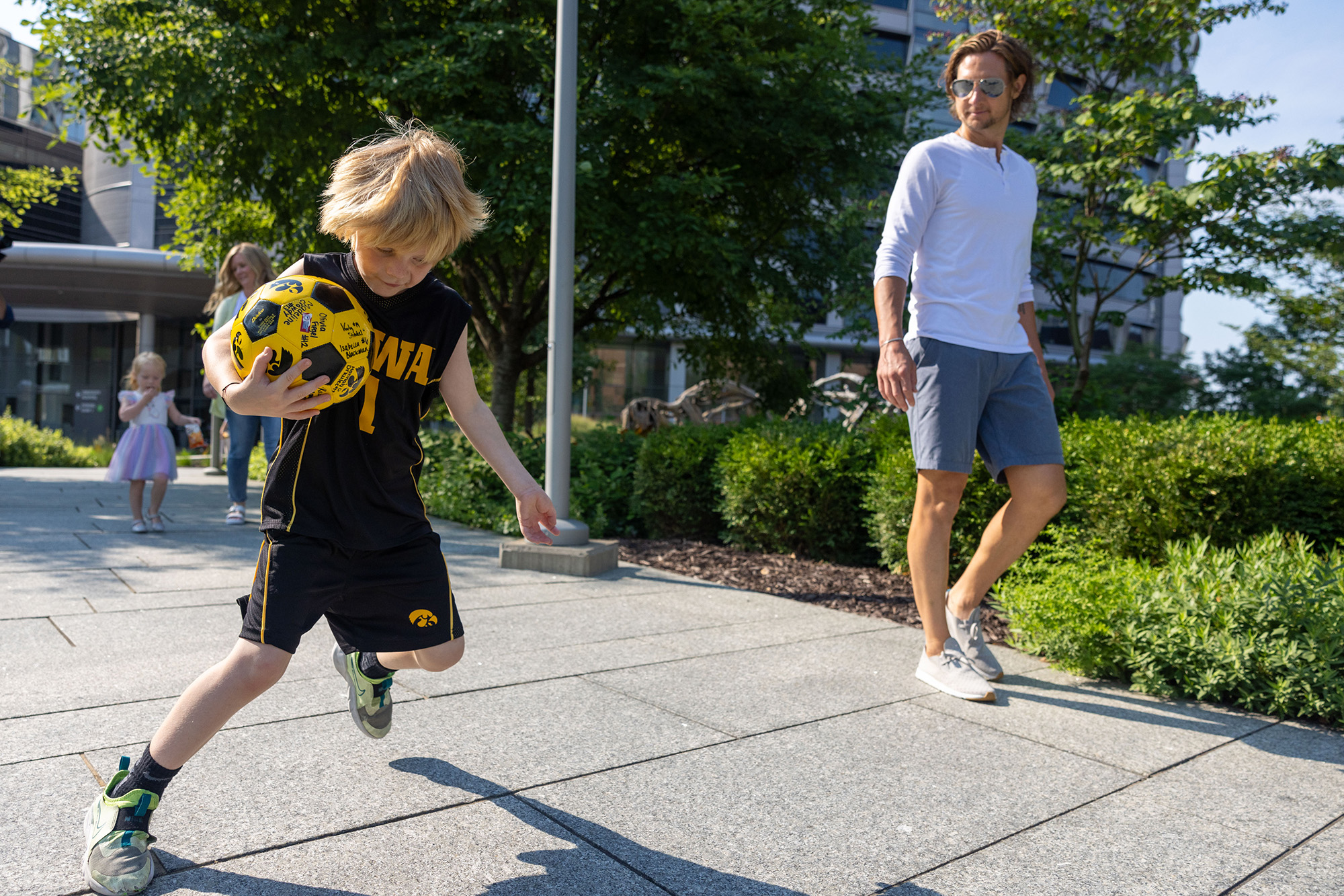 a young boy carries a ball while walking with his family on a hospital campus