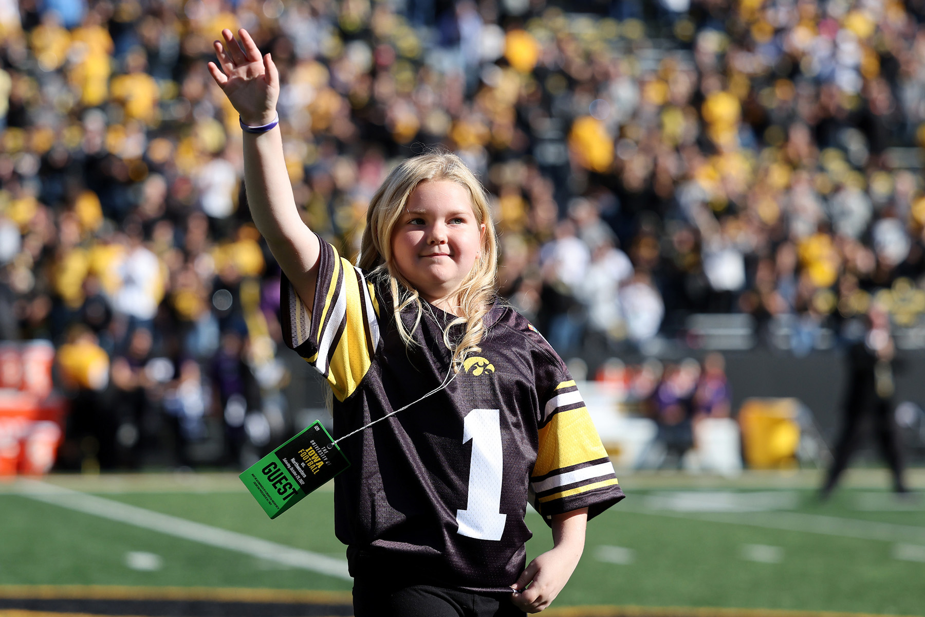 A girl standing on a football field waving to the crowd