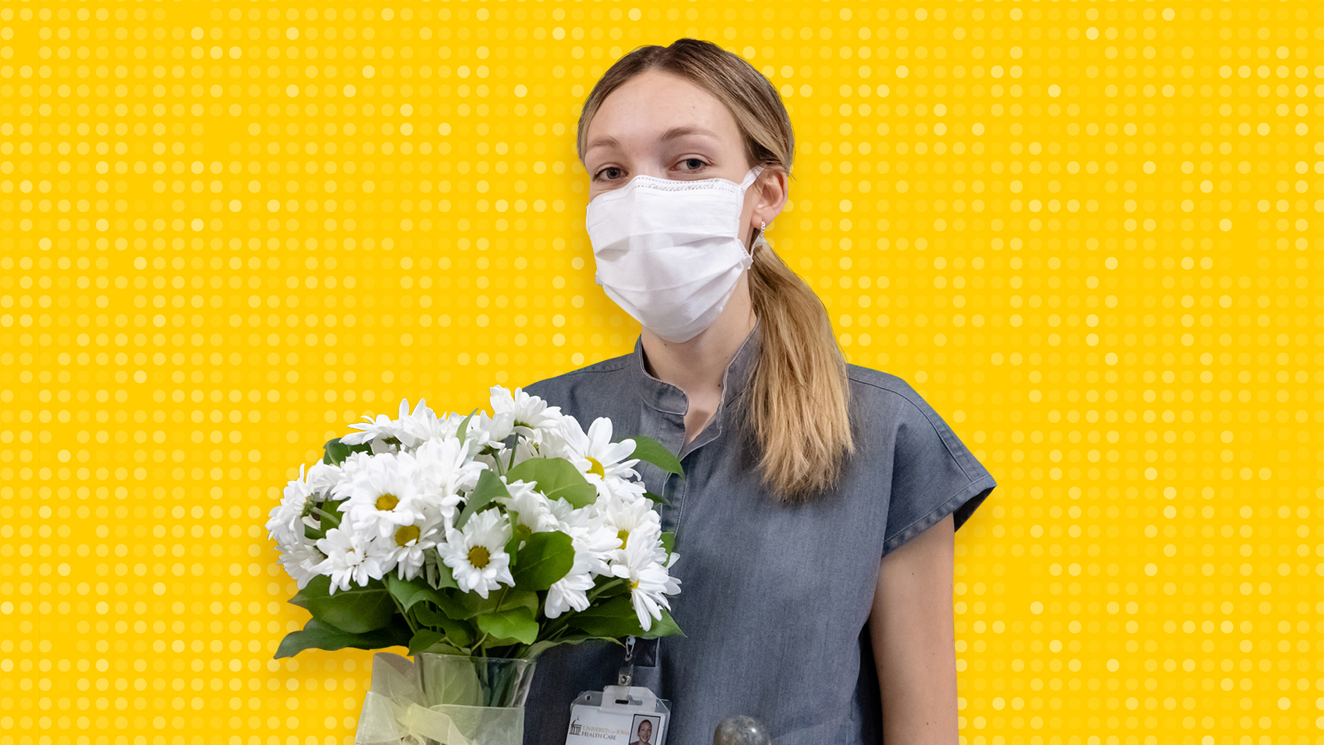 A woman holding a vase of flowers and wearing a mask