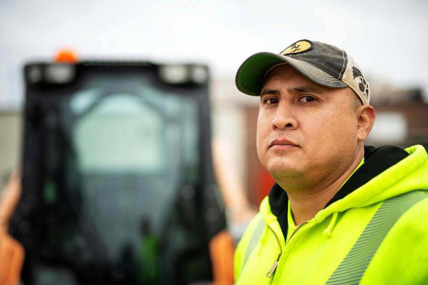 a man wearing protective reflective clothing stands near a forklift