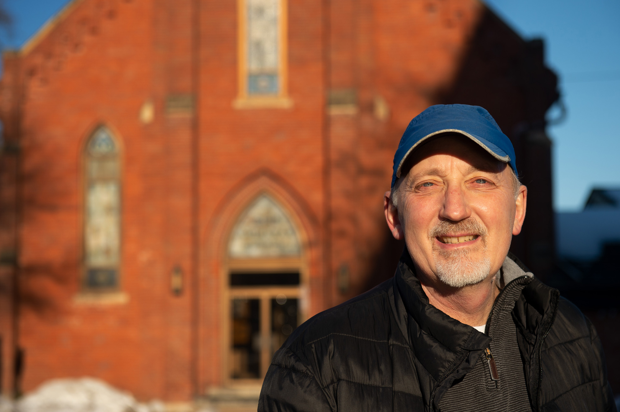 A man smiling standing in front of a brick building