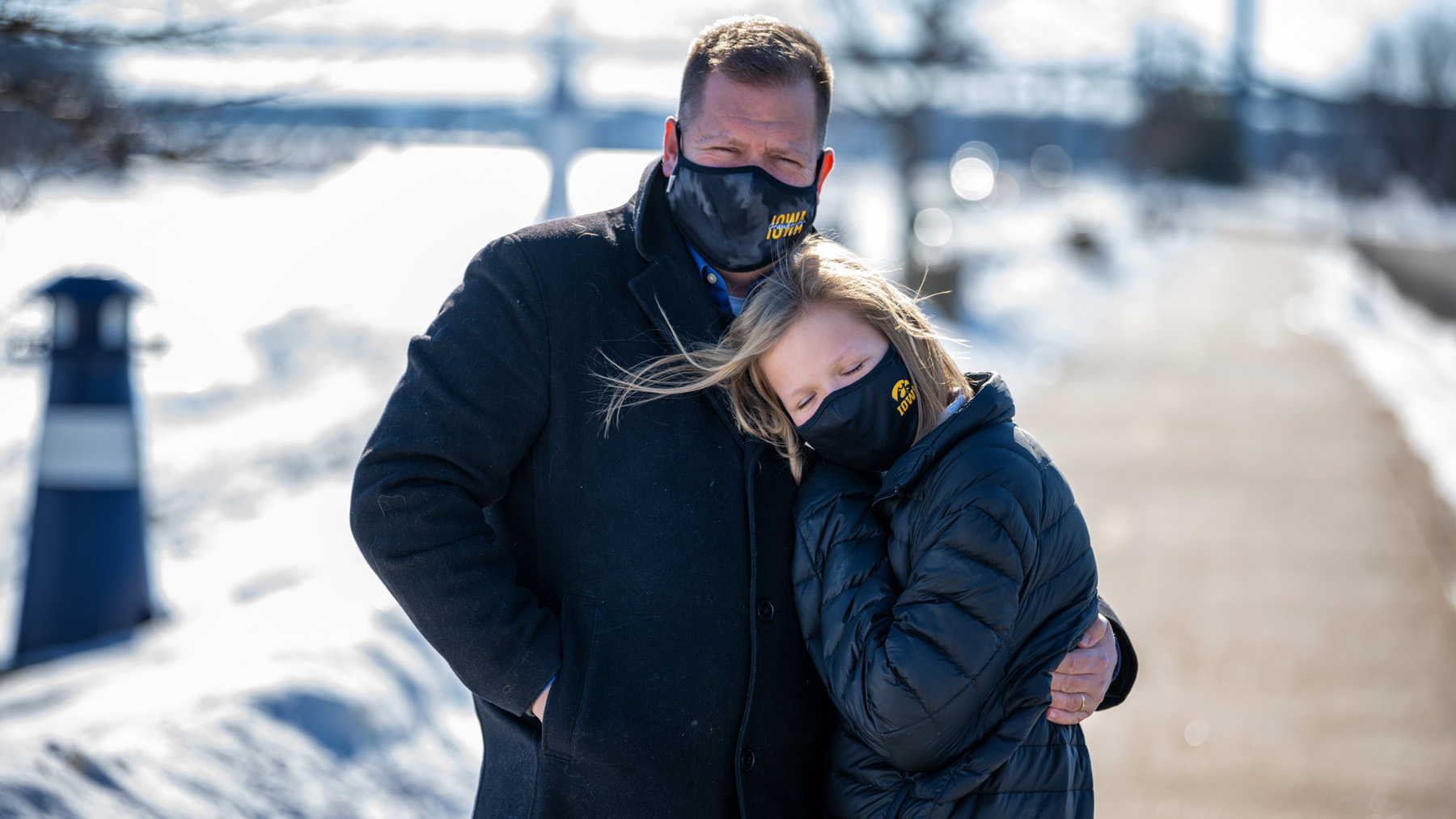 a man and daughter embrace on a sidewalk on a winter day