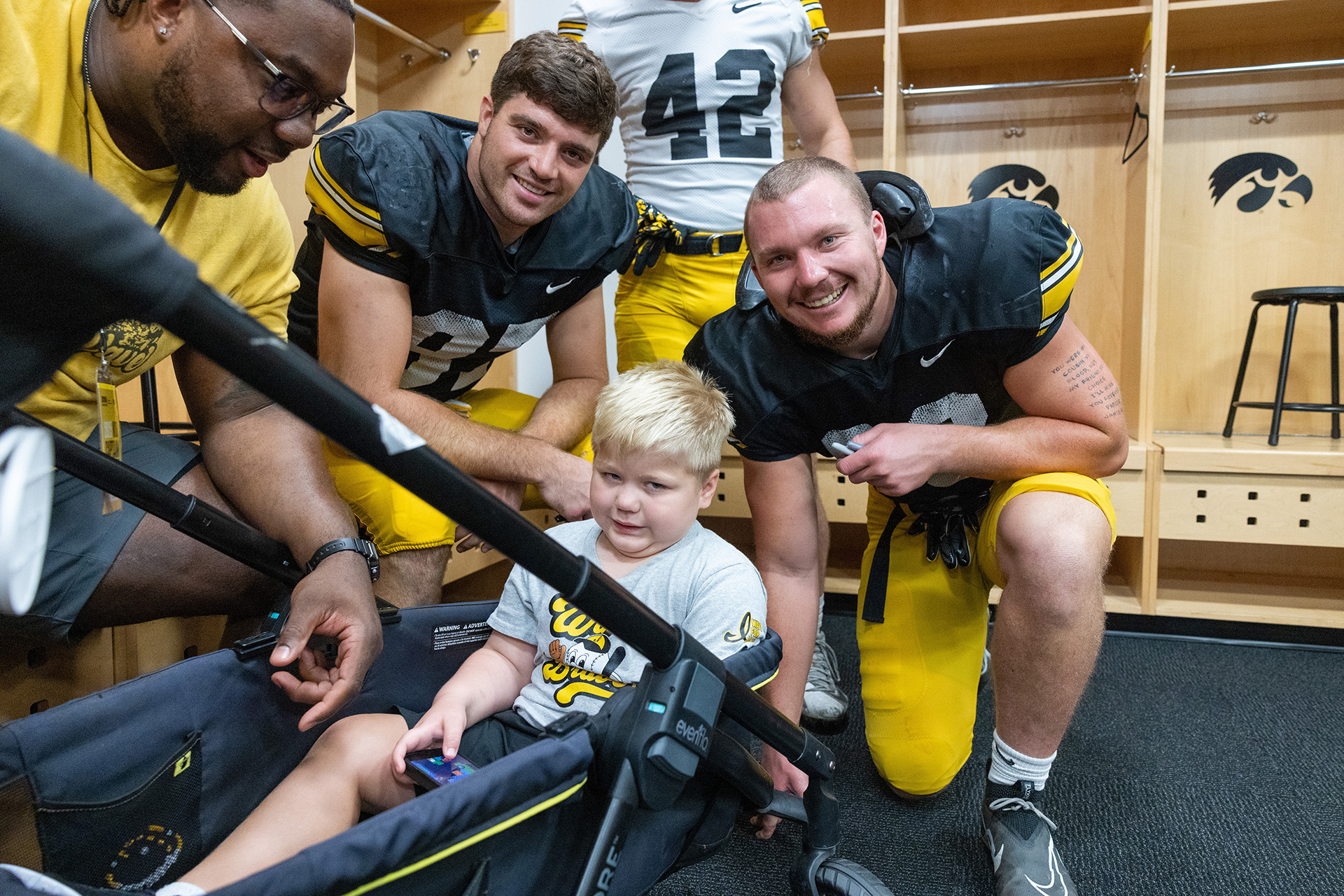 a young boy poses near two members of the iowa football team in the locker room in Kinnick Stadium