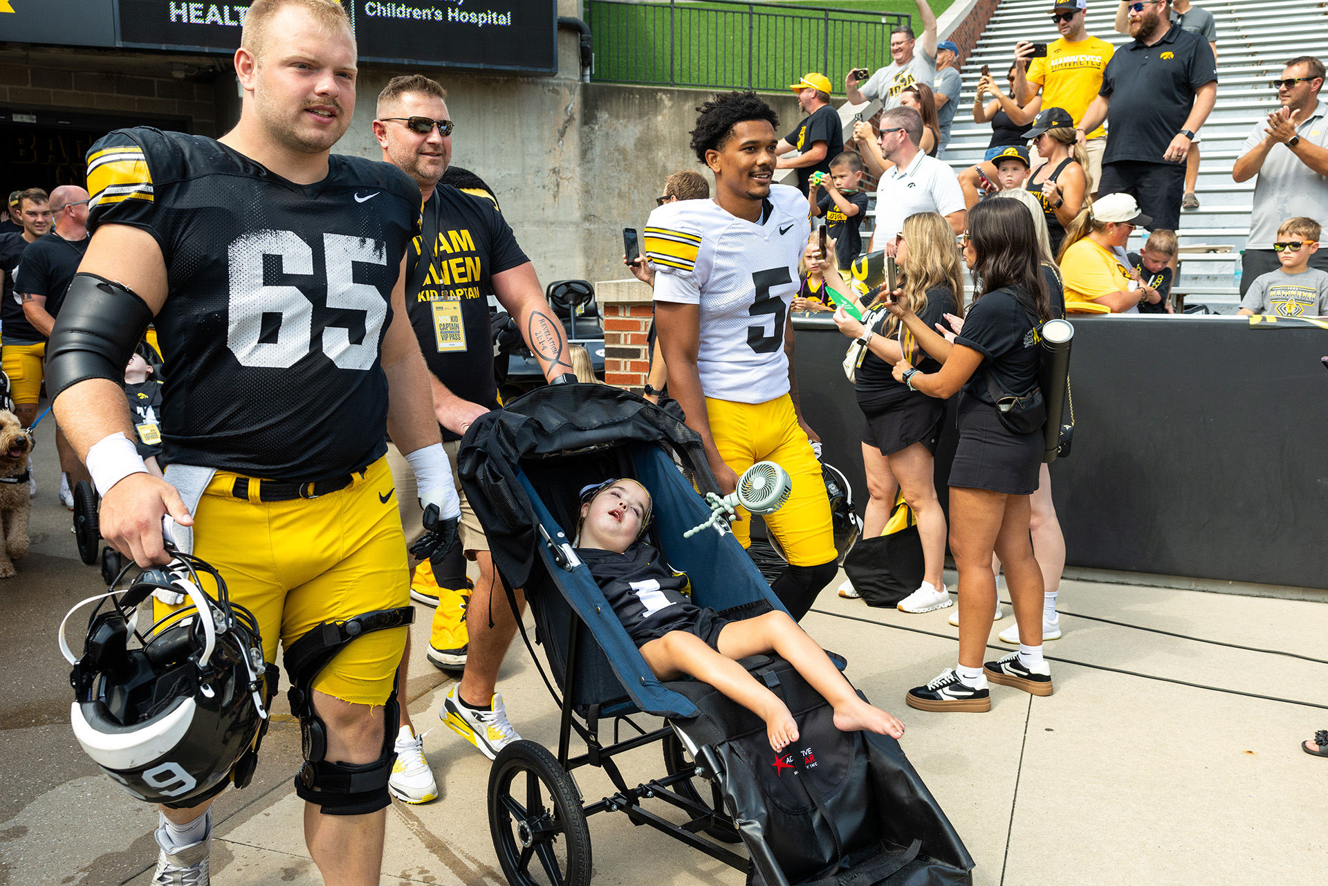 a girl is led by two Iowa football players to the field at Kinnick Stadium