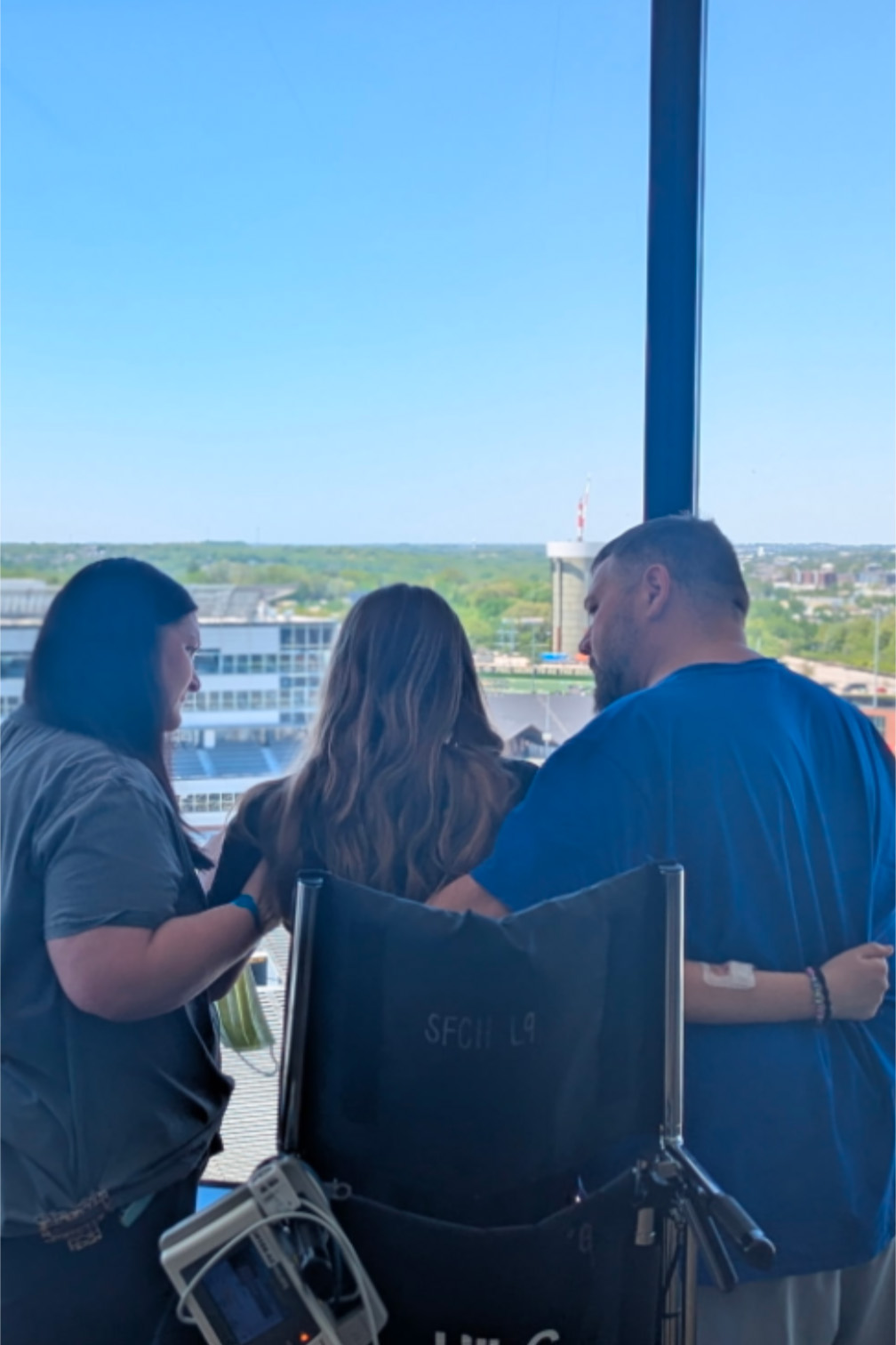 a girl and her parents look out a window at a football field below
