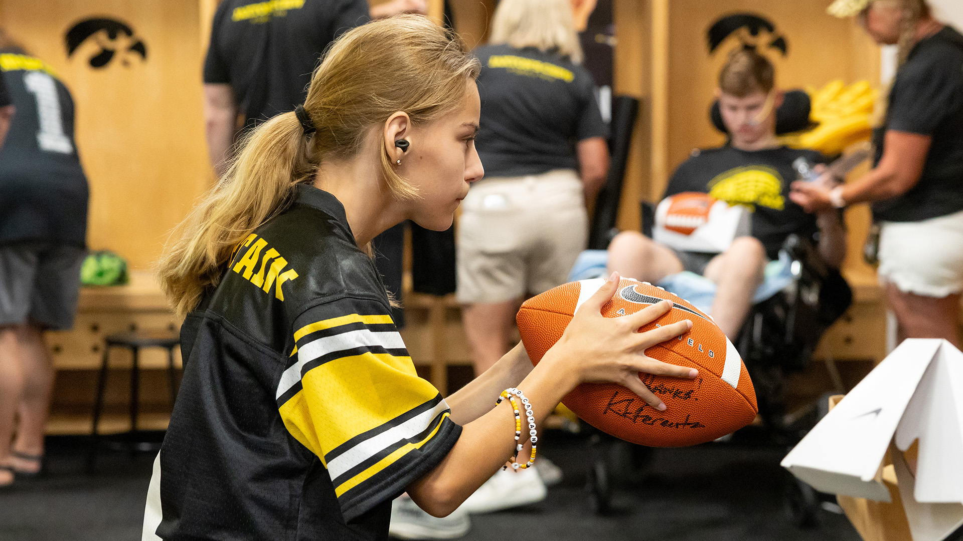 Kid Captain Lily Sebastian holding an autographed football in the locker room in Kinnick Stadium