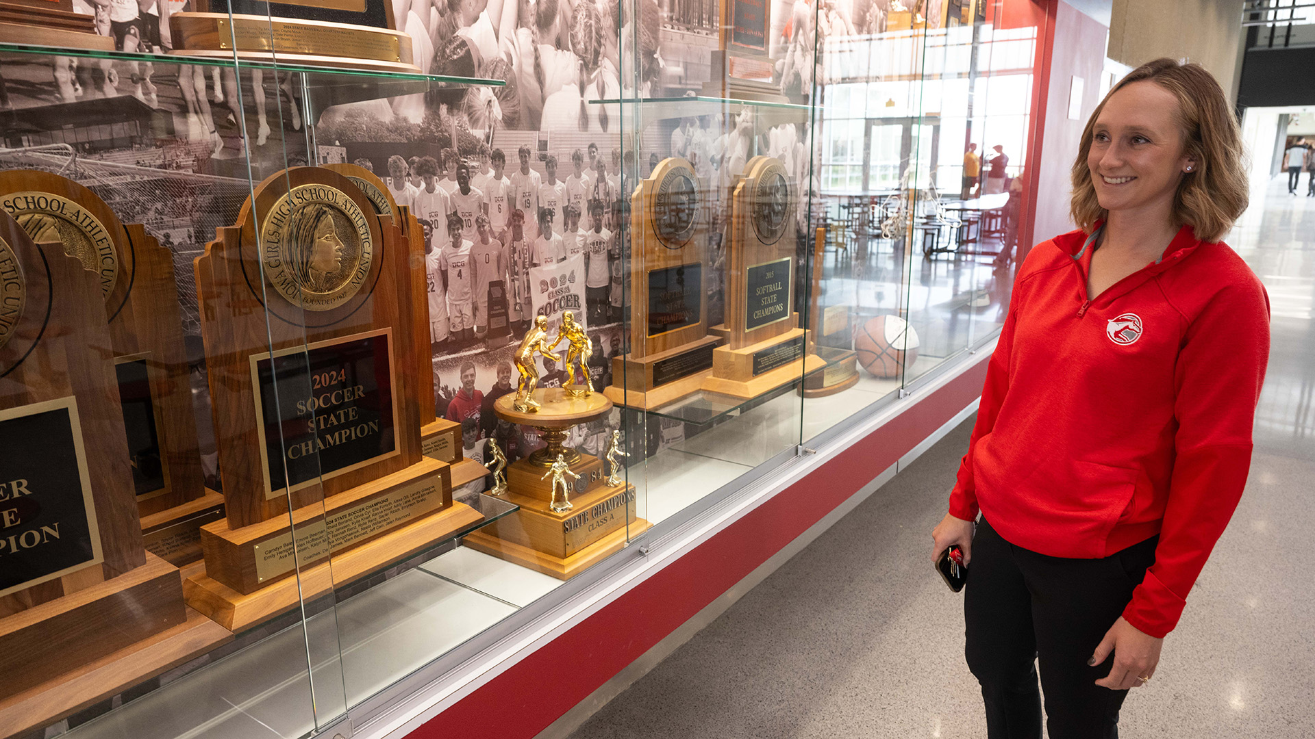 University of Iowa alum Madison Melchert stands near the trophy case at Dallas Center-Grimes High School