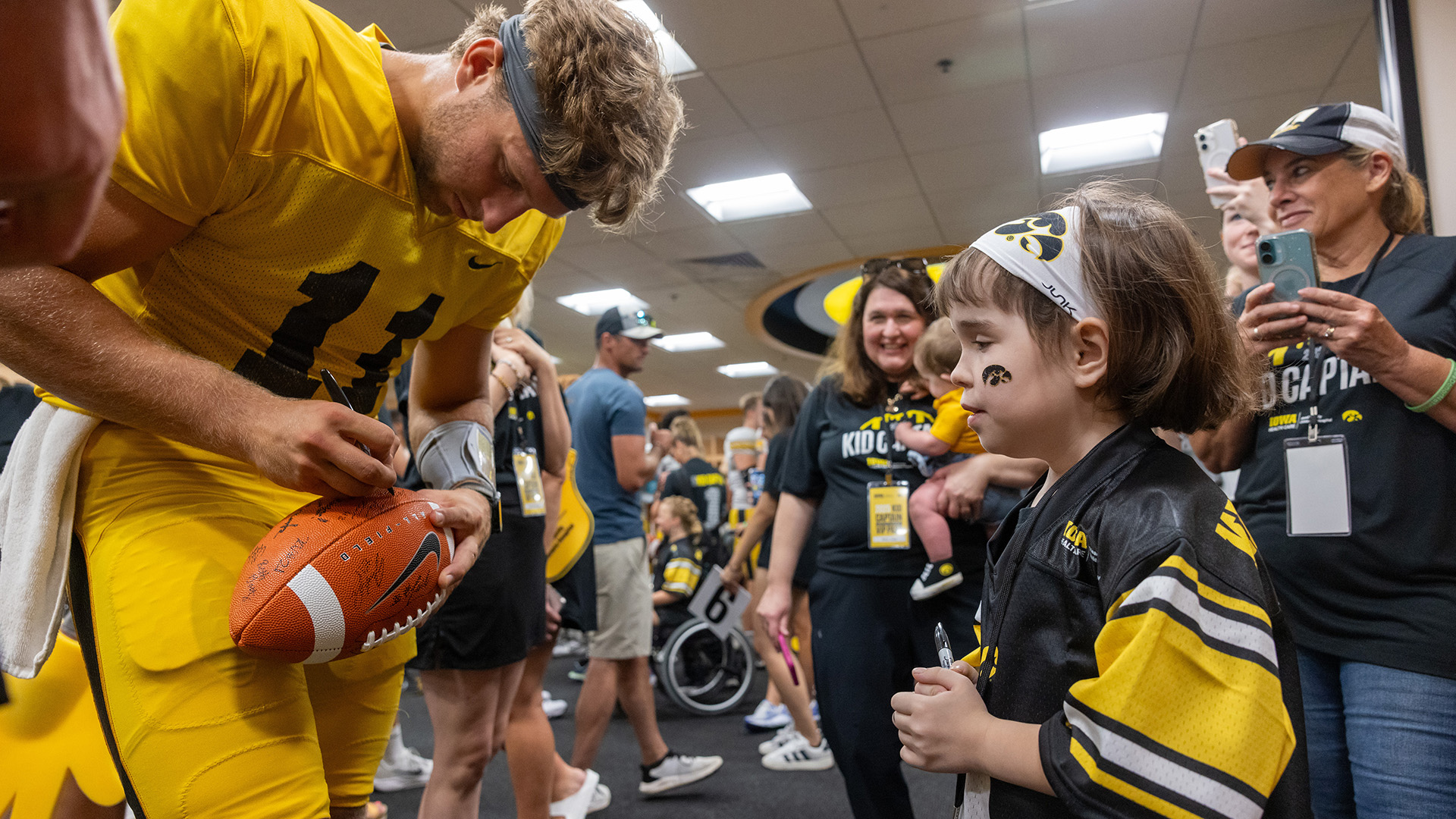 Mark Gronowski autographs a football for Kid Captain Millie Judge in the Iowa Hawkeyes' locker room at Kinnick Stadium