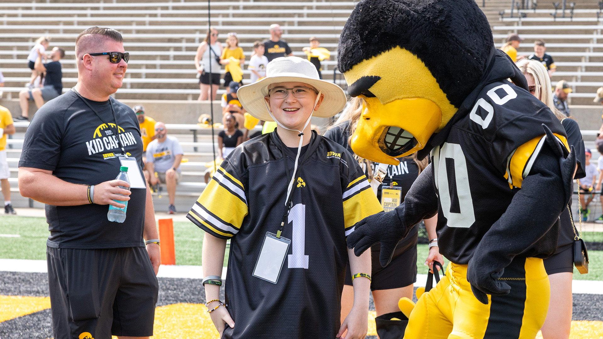 a boy in a hawkeyes jersey hangs out on the football field with Herky during Kids Day at Kinnick
