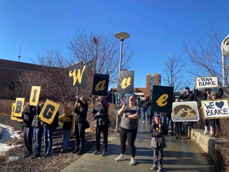 people standing outdoors holding signs and waving to a patient at a children's hospital