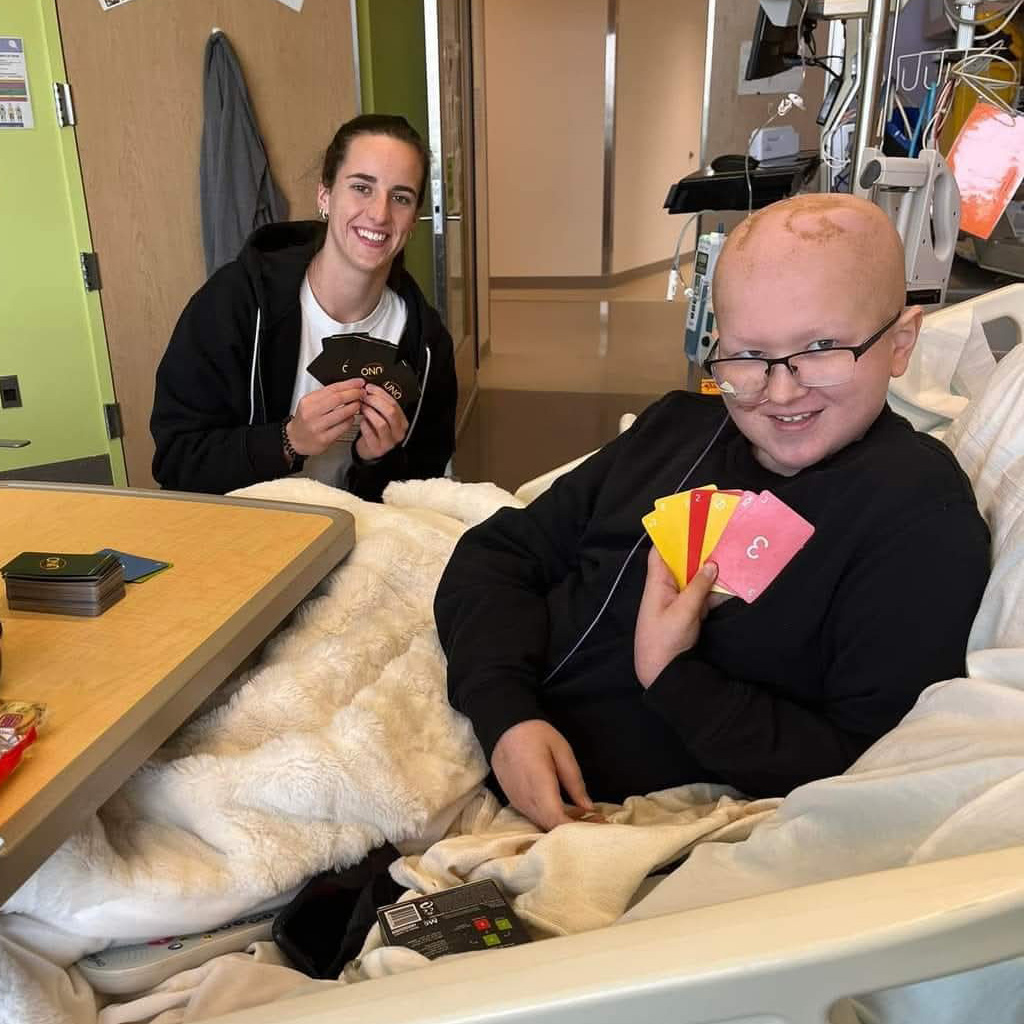 a young boy plays uno with basketball star Caitlin Clark in the hospital