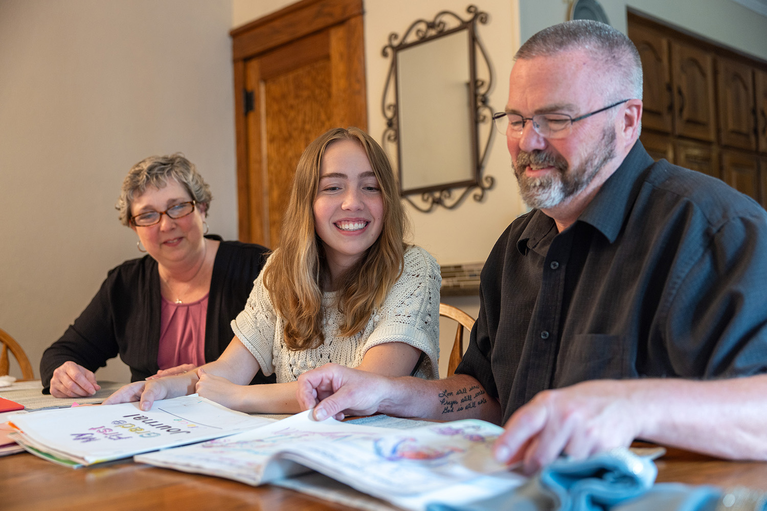 a young woman sitting between her parents at a table, as they look at a book on the table