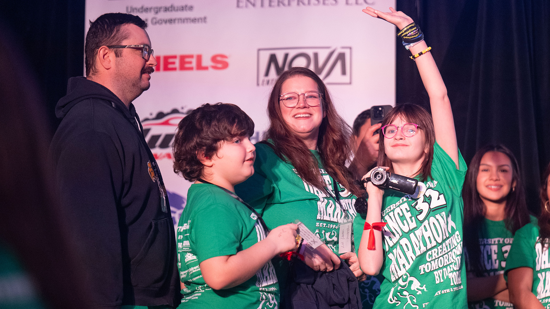 a young girl at UI Dance Marathon's Big Event waves to the dancers from a stage while her mom, dad, and brother stand next to her