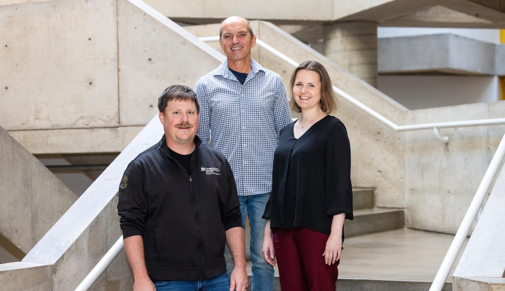three researchers stand on a staircase