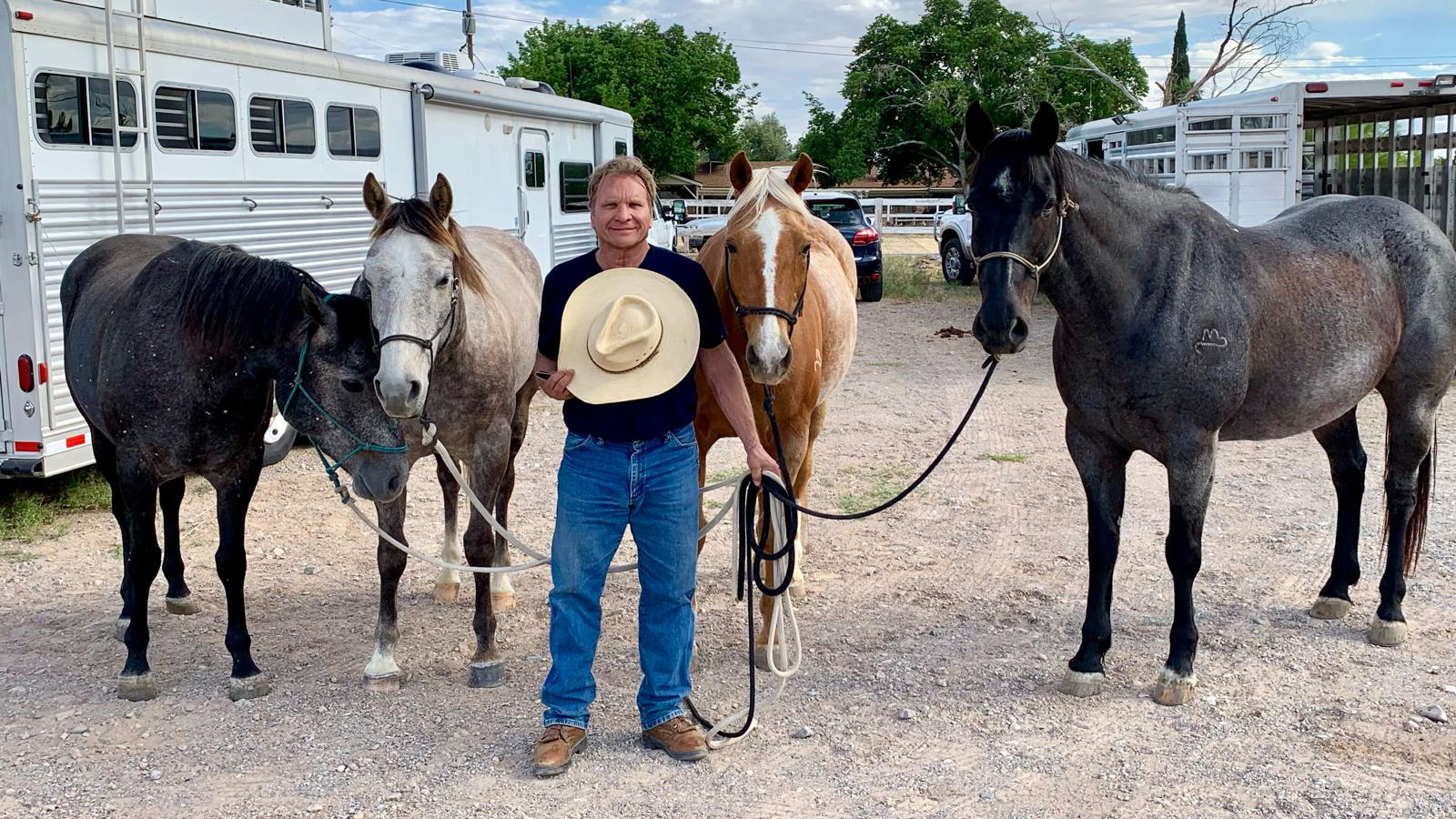 a man holding a cowboy hat stands with four horses