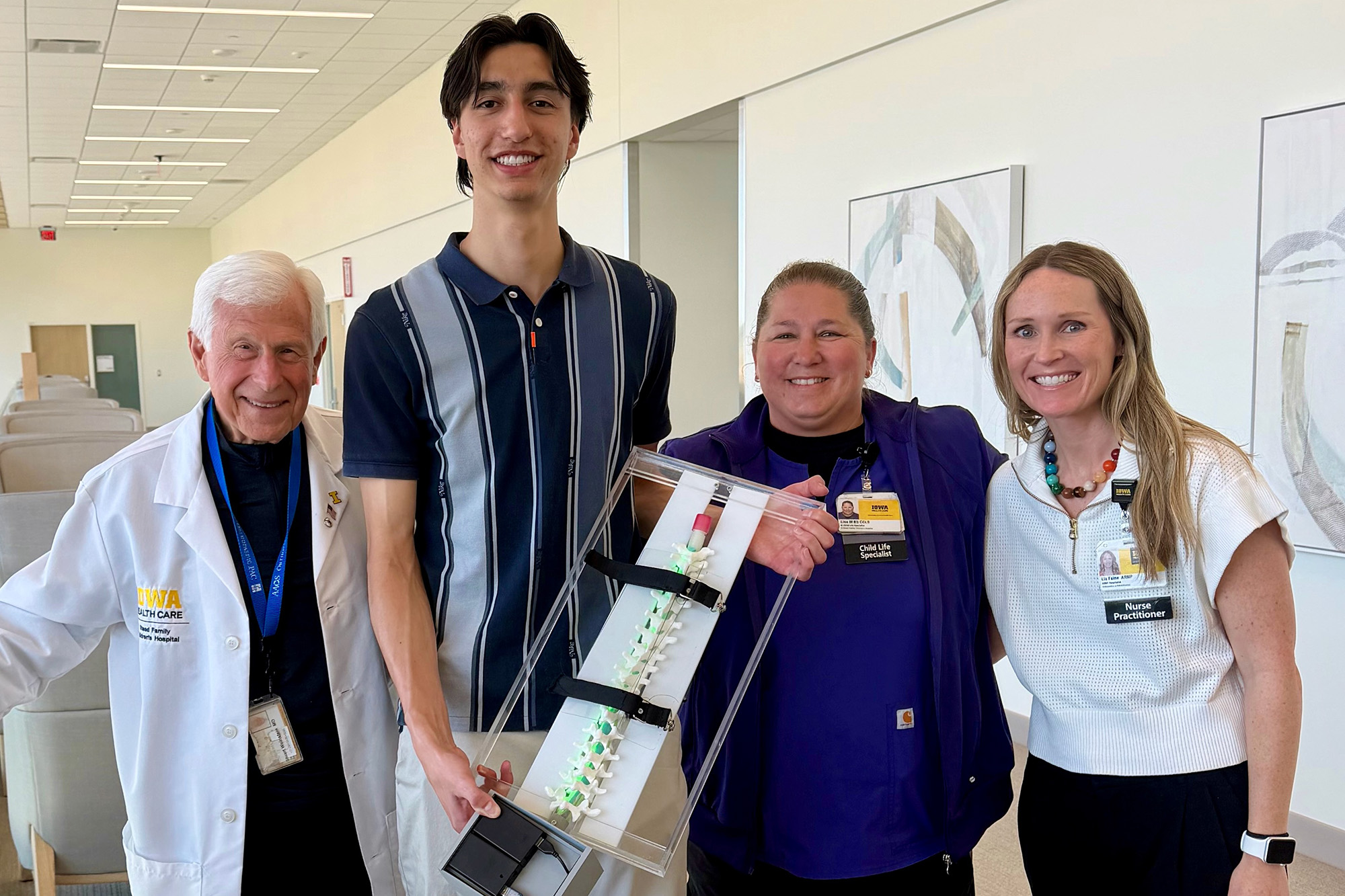 four people standing in a hallway; one of the people holds a spine model