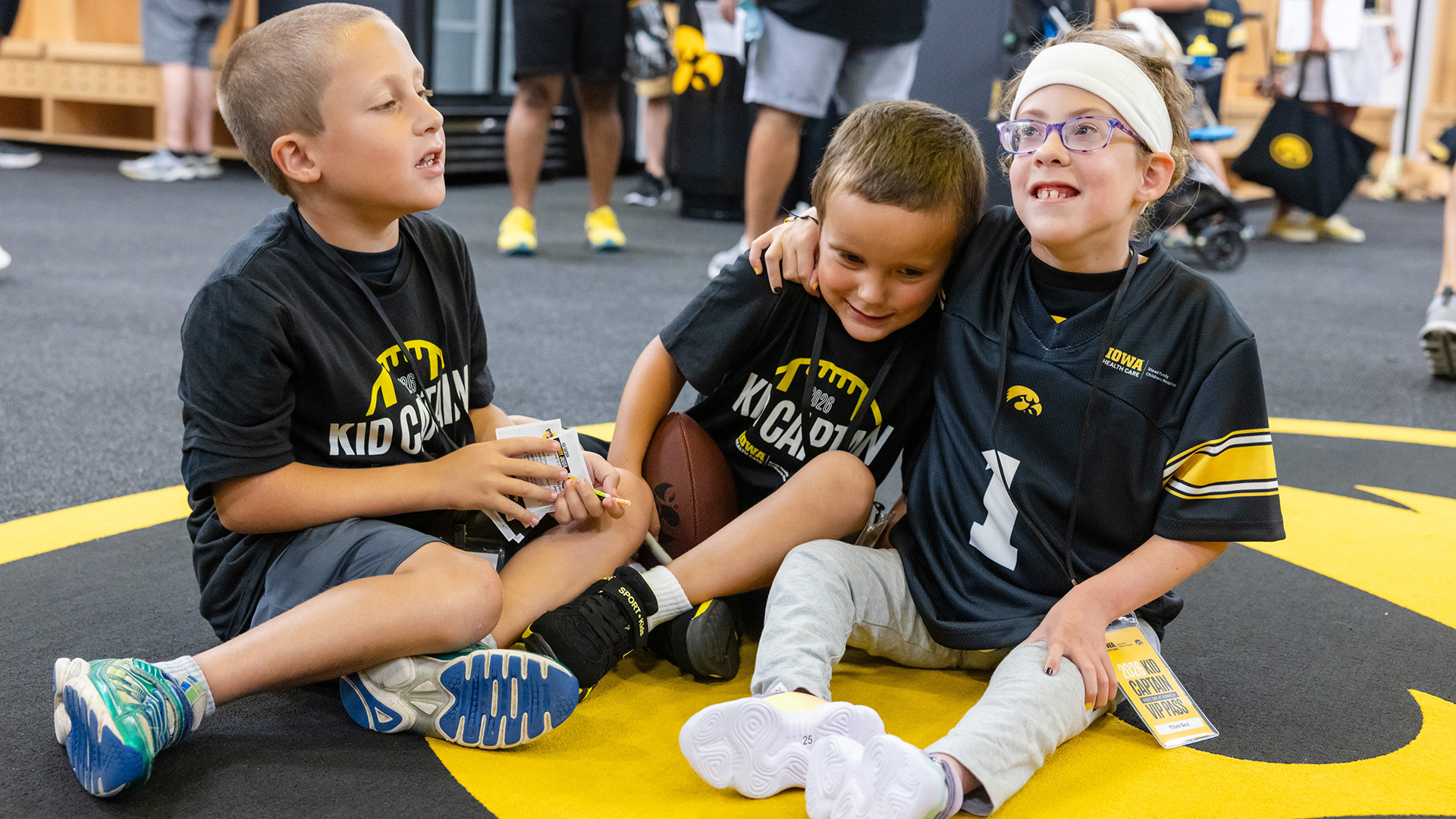 three siblings sitting together on the floor of the Iowa Hawkeyes locker room