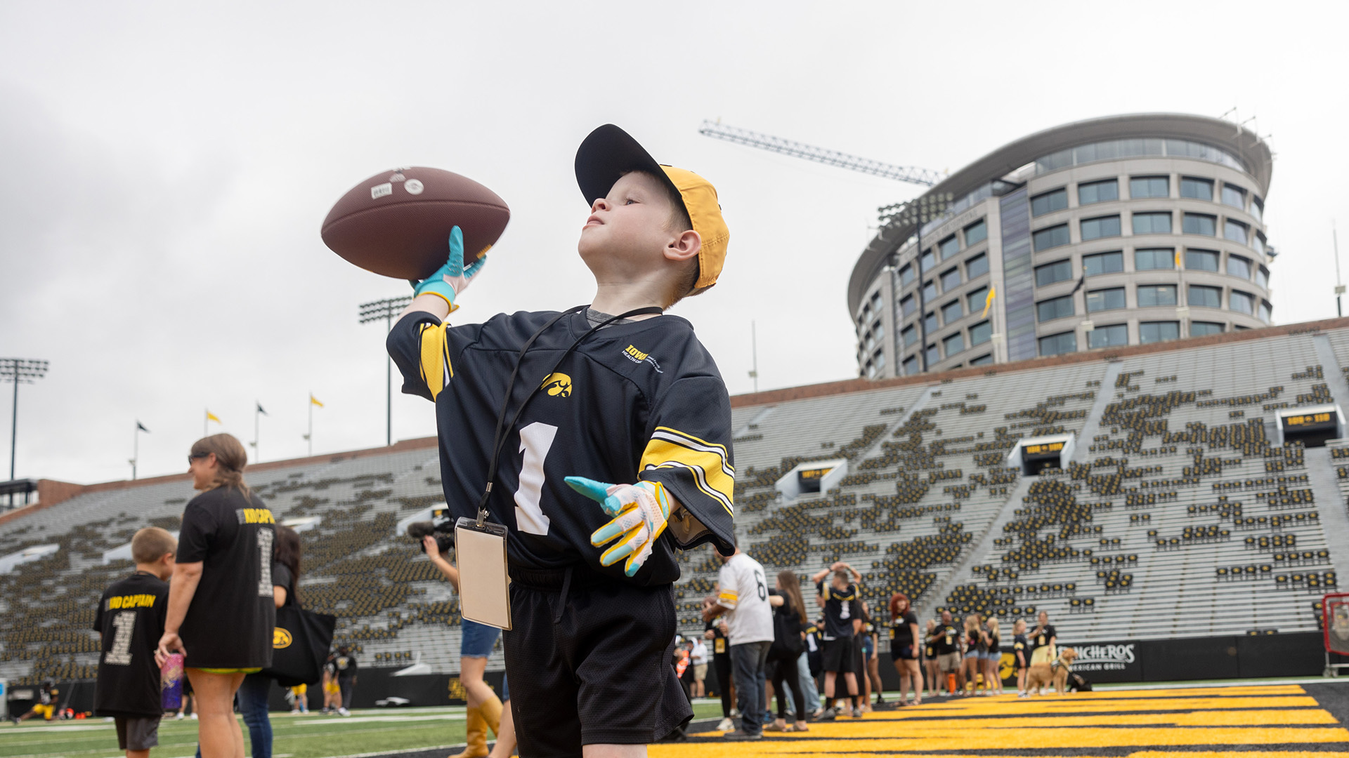 a young boy throws a football at Kinnick Stadium; the UI Health Care Stead Family Children's Hospital is visible in the background